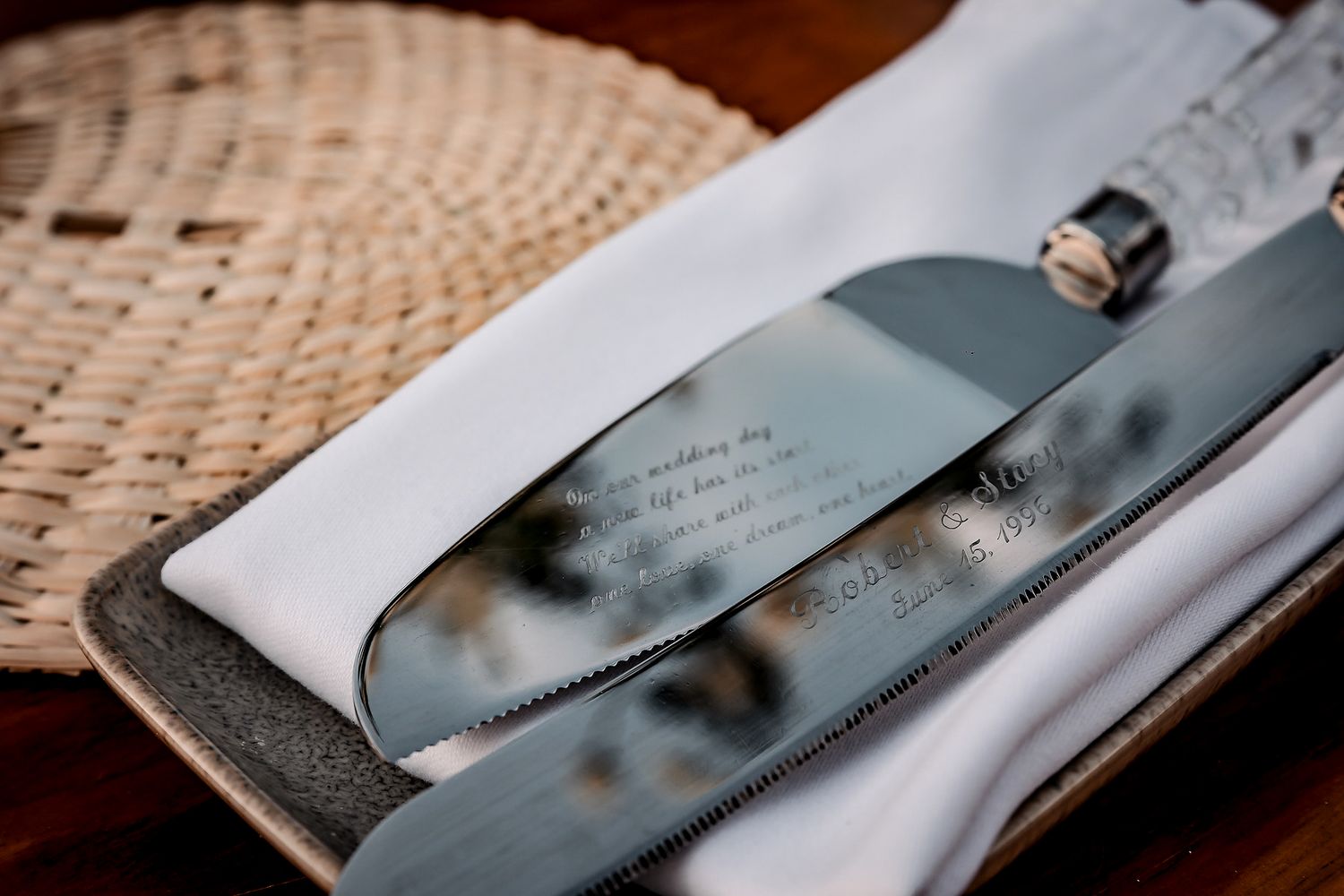 Engraved wedding cake knife and server set resting on white napkin with wicker placemat background.