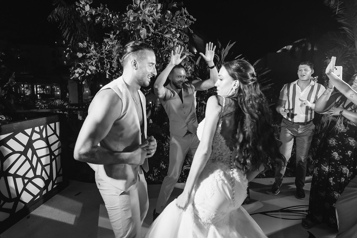 Black and white photo of bride and groom dancing joyfully at outdoor wedding reception with guests celebrating.