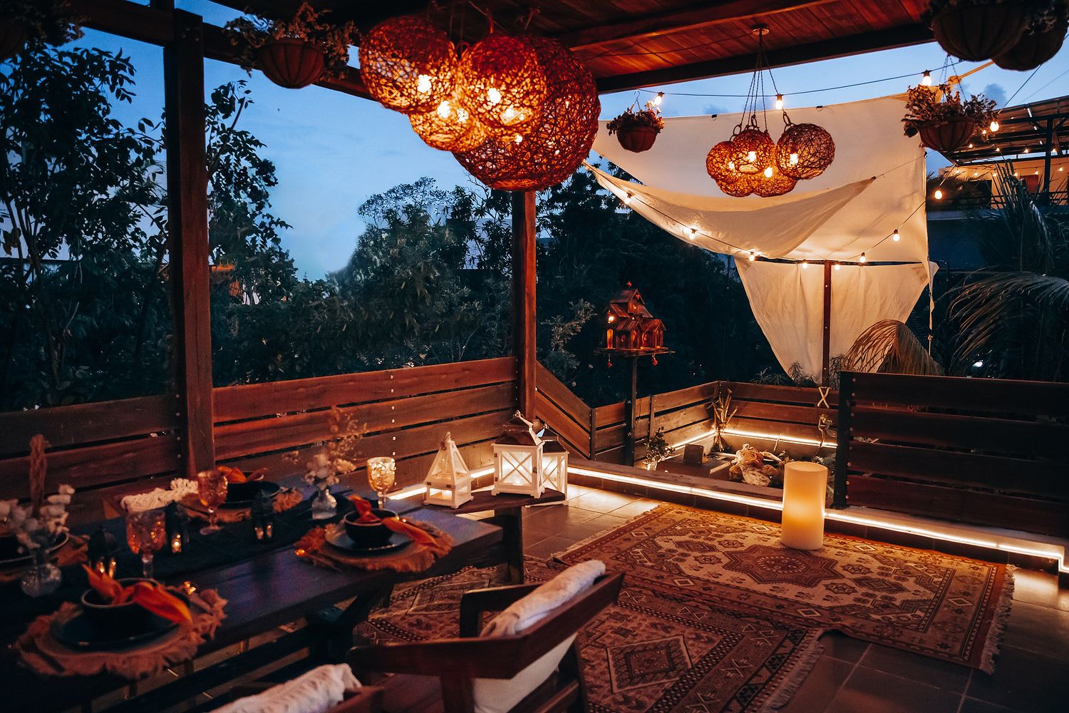 Cozy boho outdoor pavilion with glowing rattan lights, low table dining, and draped canopy at night.
