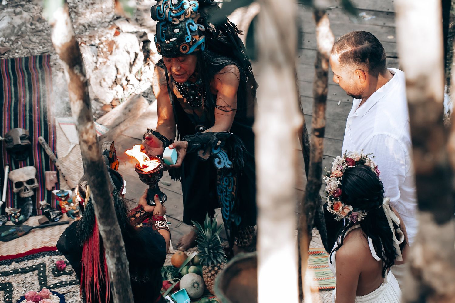 People in ceremonial dress participate in a traditional ritual under a forest canopy.