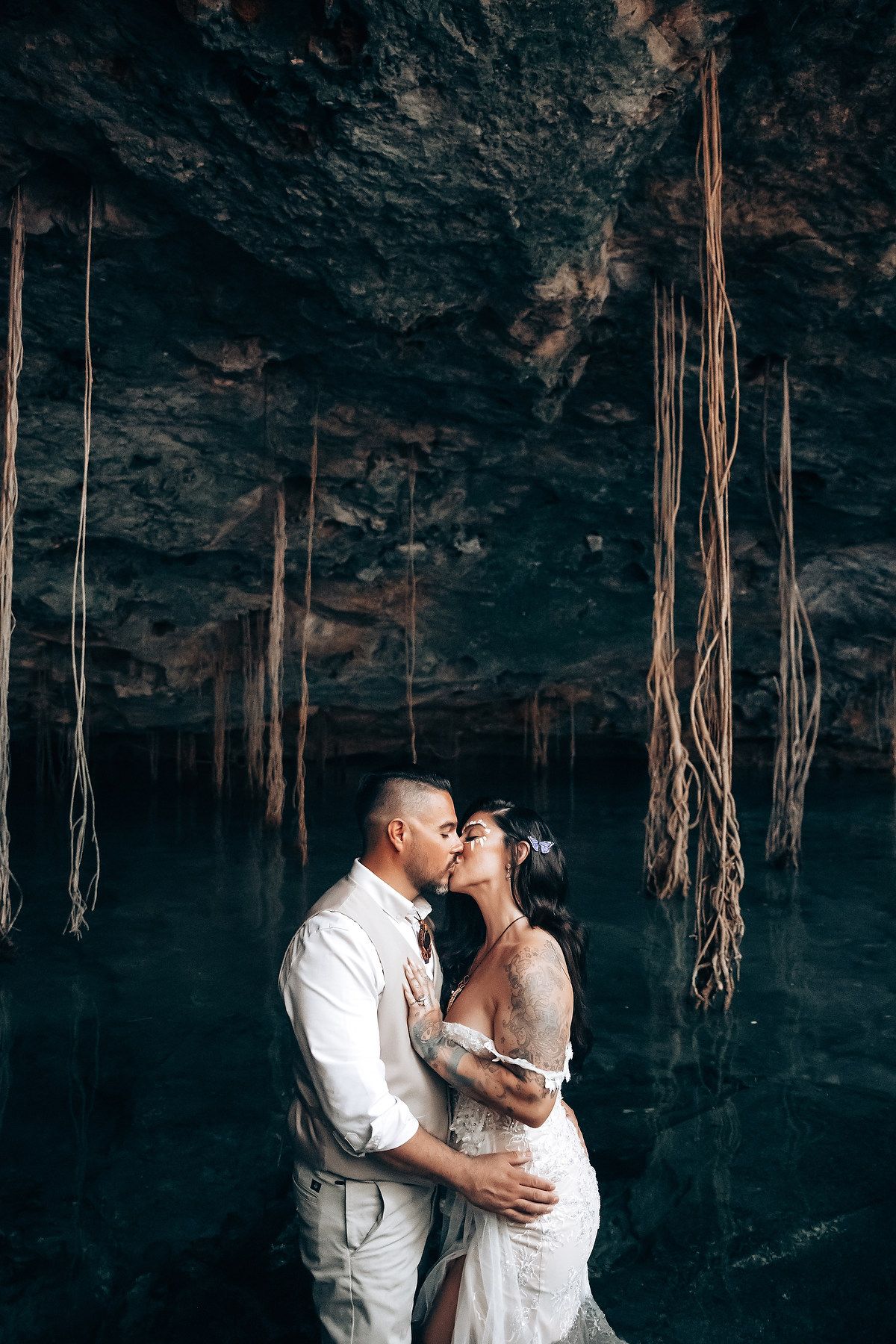 A romantic embrace captured in a dramatic cave setting with hanging roots in the background.