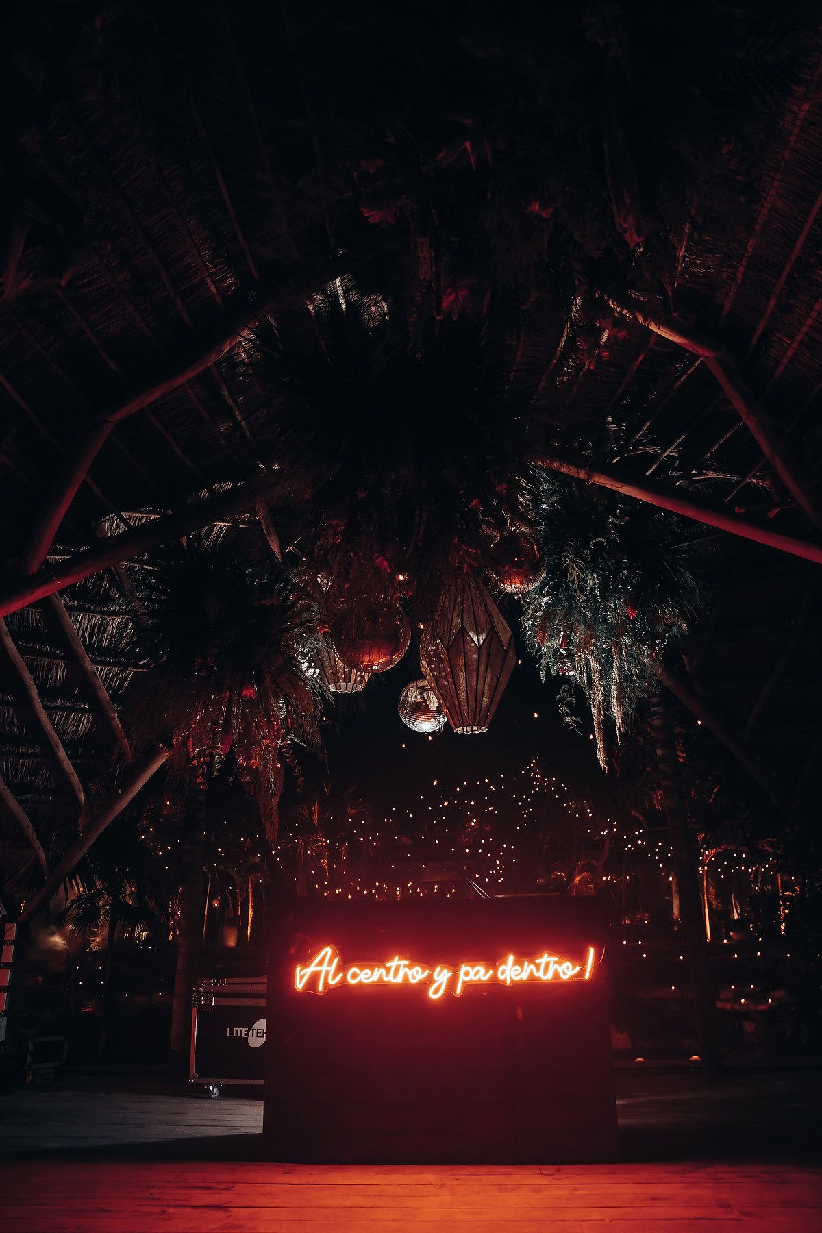 Outdoor nighttime scene with red neon sign illuminating palm trees and string lights.
