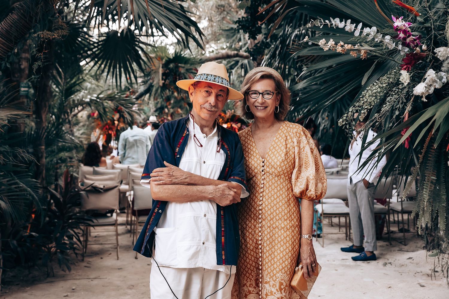 Guests in vibrant patterns and traditional attire socializing at an outdoor tropical celebration.