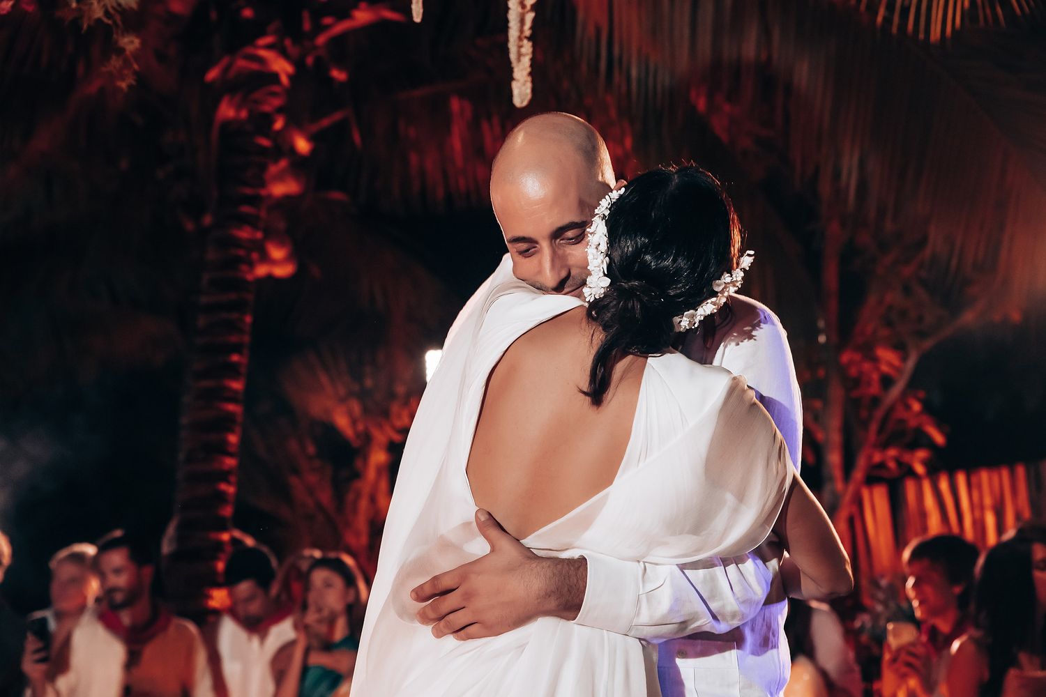 Wedding guests enjoying themselves on a dance floor with red ambient lighting and palm decorations.