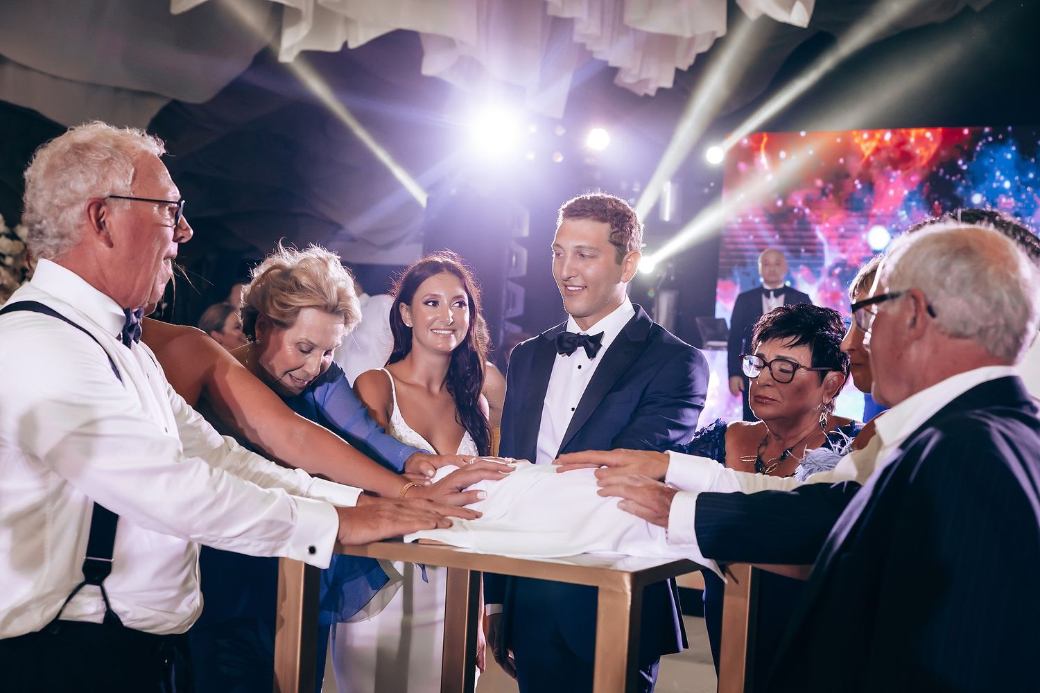 Wedding reception dance floor filled with guests under dramatic lighting and white ceiling decor.