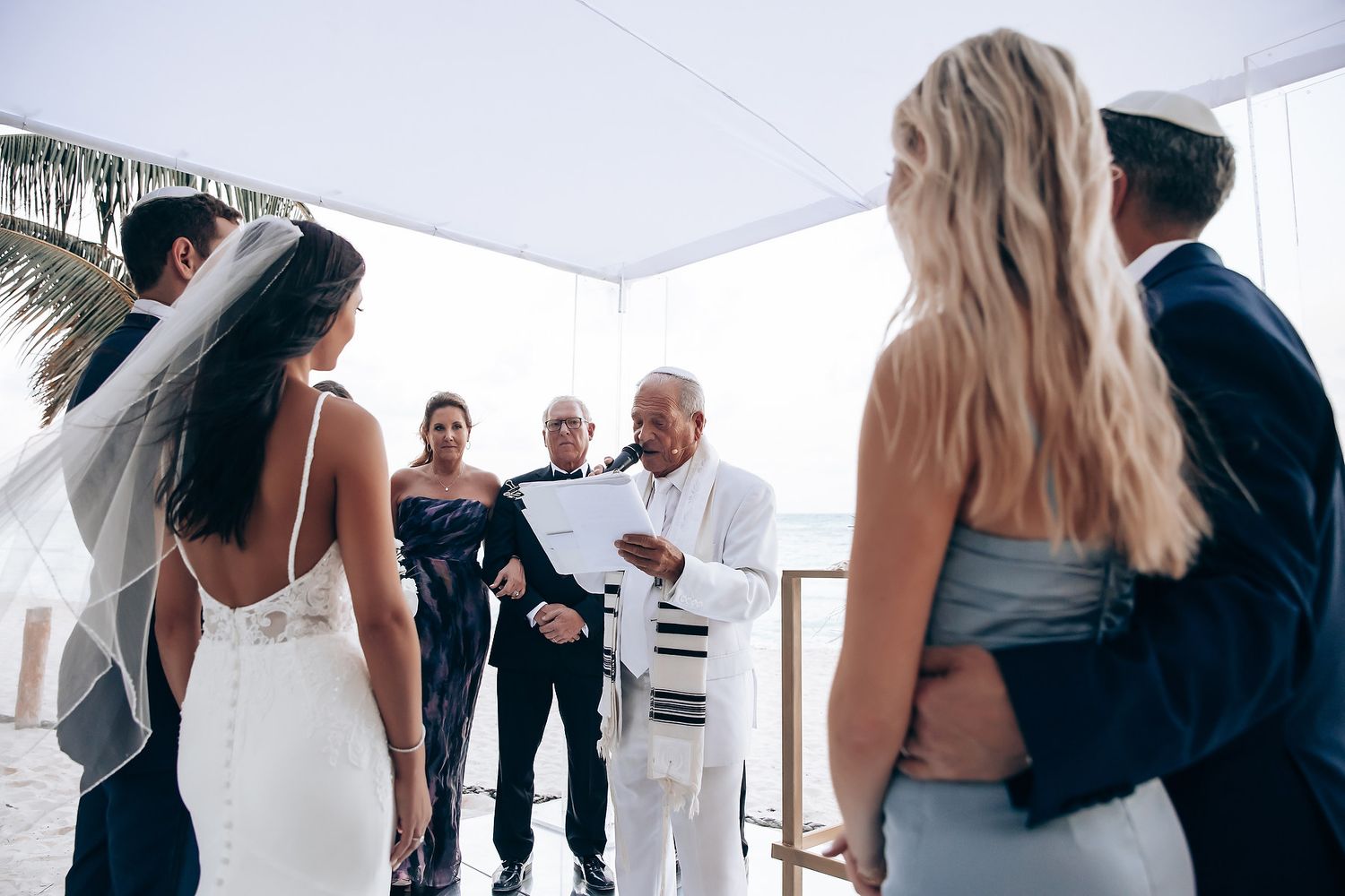 Wedding guests mingling under white tent at outdoor reception.