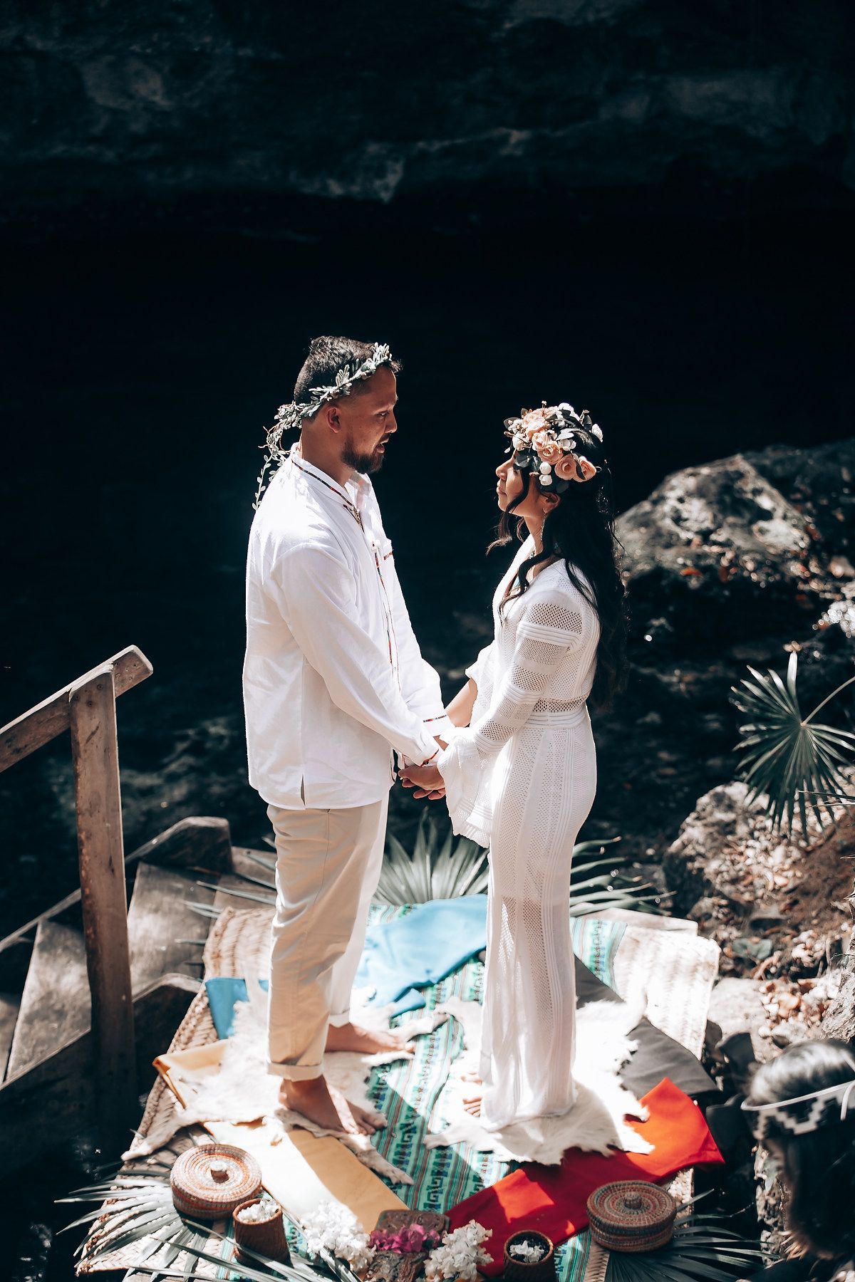 Traditional ceremony participants dressed in white performing rituals in a natural outdoor setting.