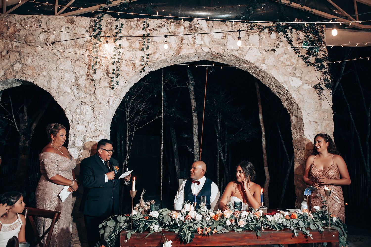 A wedding reception dinner setup under rustic stone arches with floral table decorations.