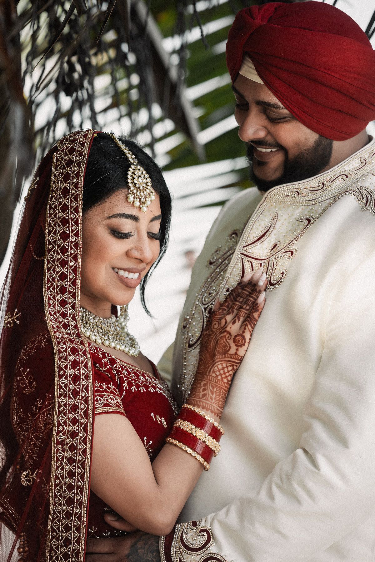 Sikh bride and groom in traditional red and white wedding attire sharing a joyful intimate moment.