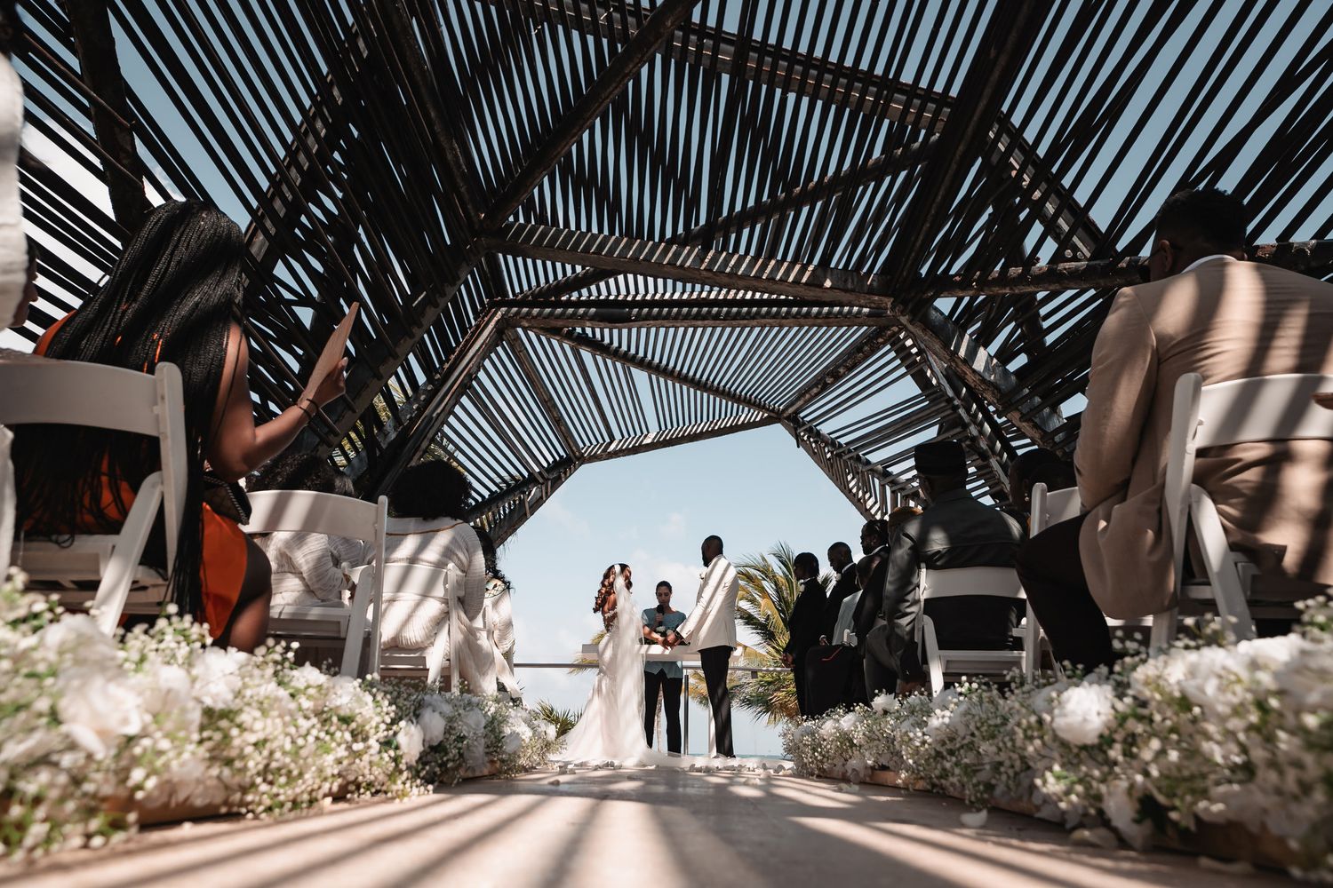 Couple exchanging vows under stunning geometric wooden arch structure at modern outdoor wedding ceremony.