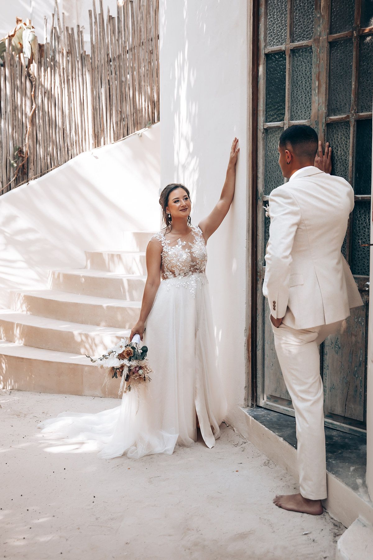 A dreamy wedding photoshoot against a white wall with tropical decor and natural lighting.