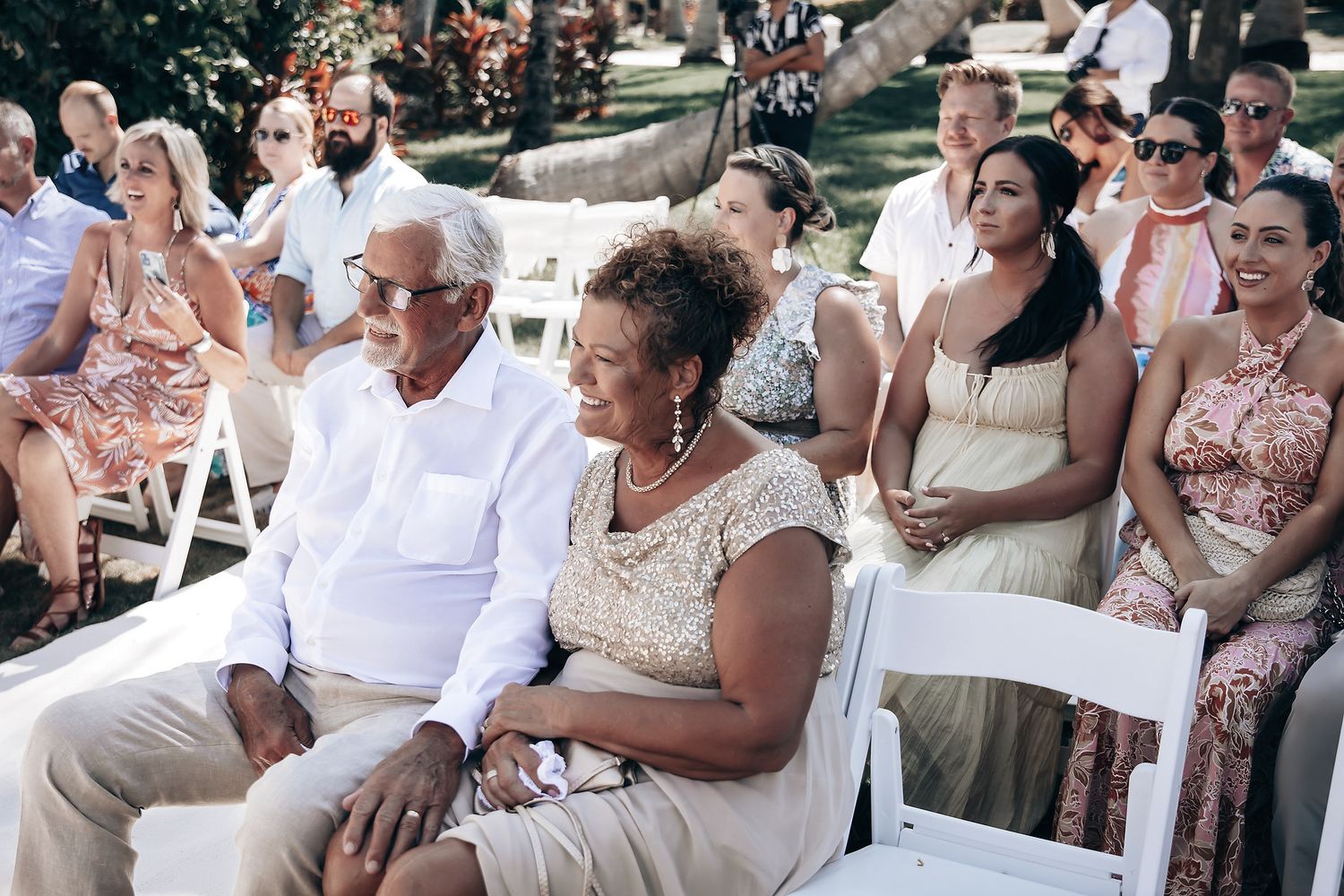 A group of people, mostly older adults, sitting in chairs at what appears to be an outdoor event or wedding.