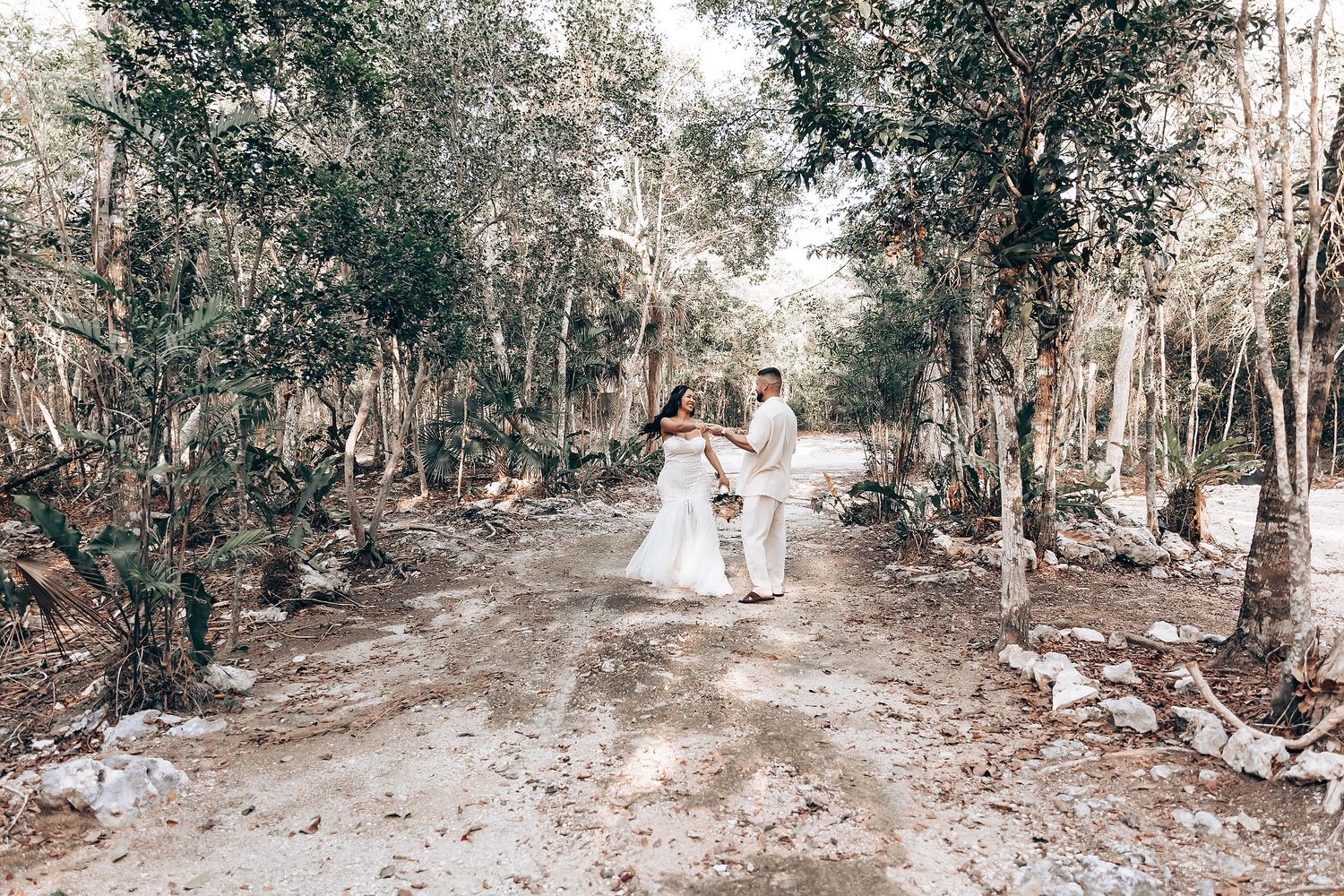 A couple walks hand in hand through a serene forest path in wedding attire.