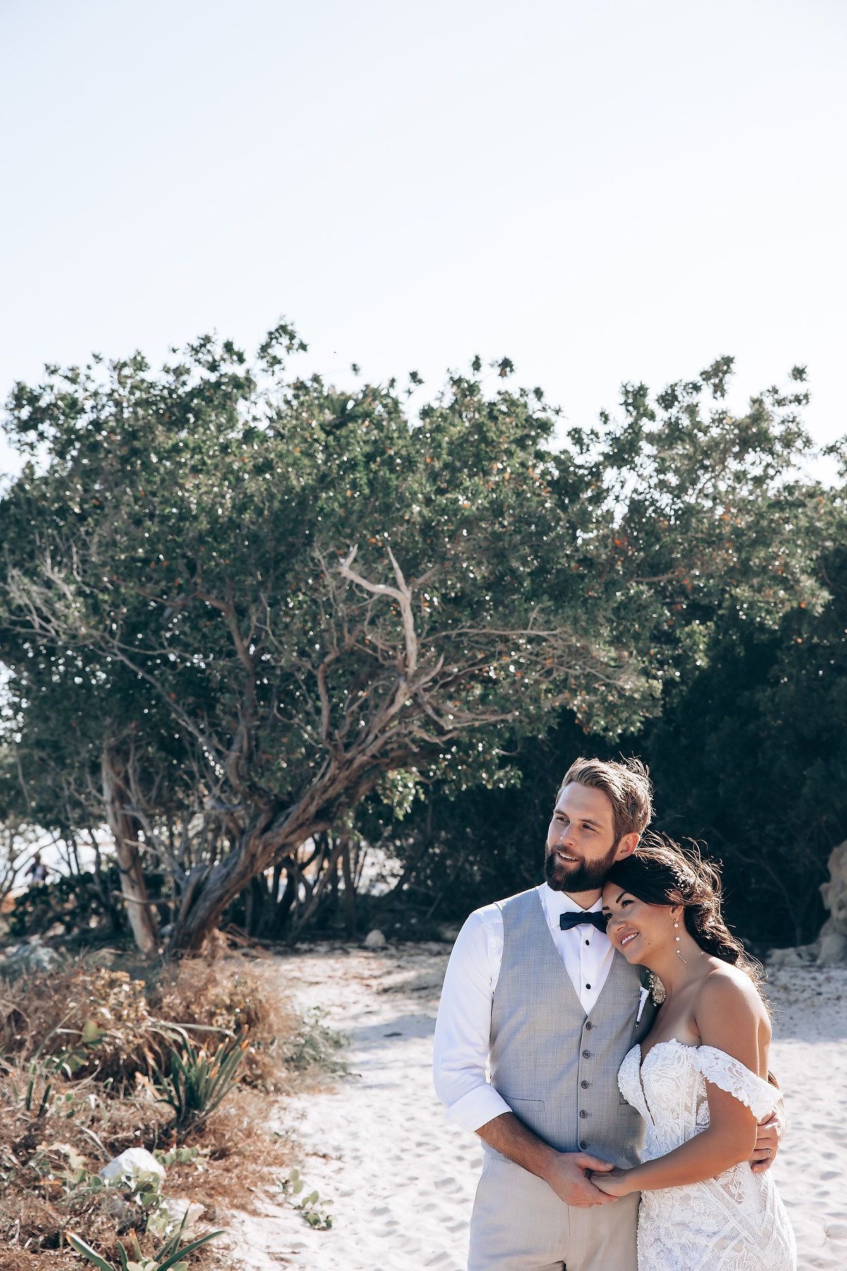 Couple walking together on a sandy beach path lined with trees.