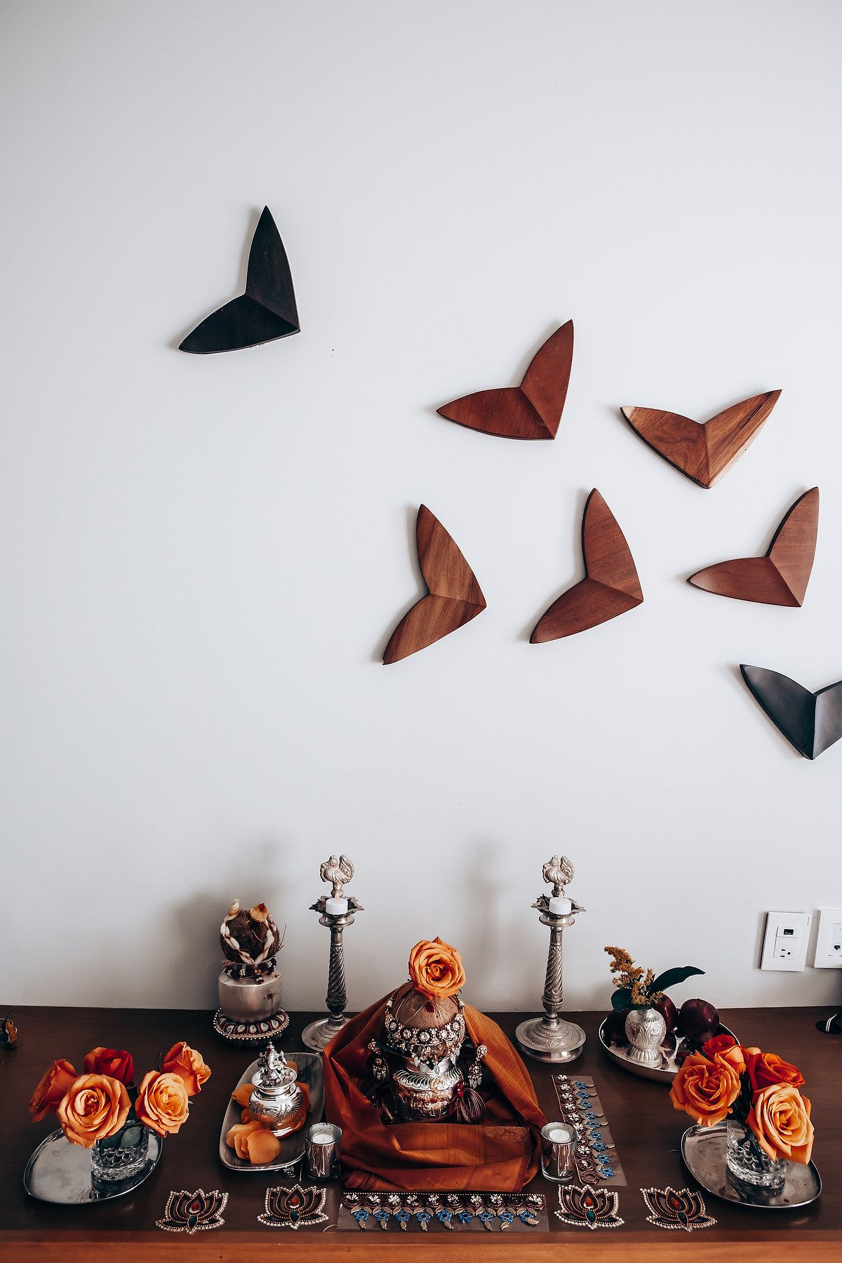Halloween-themed decorative display with wooden butterfly wall art and orange roses on dark table.