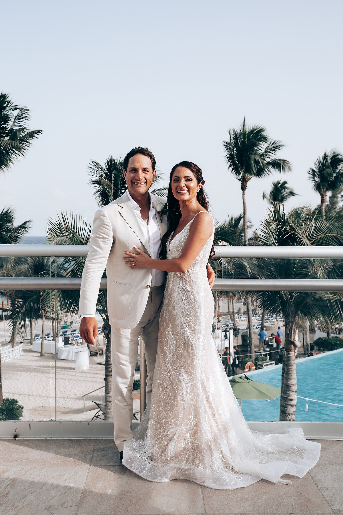Destination wedding portrait on a tropical balcony overlooking palm trees and ocean views.