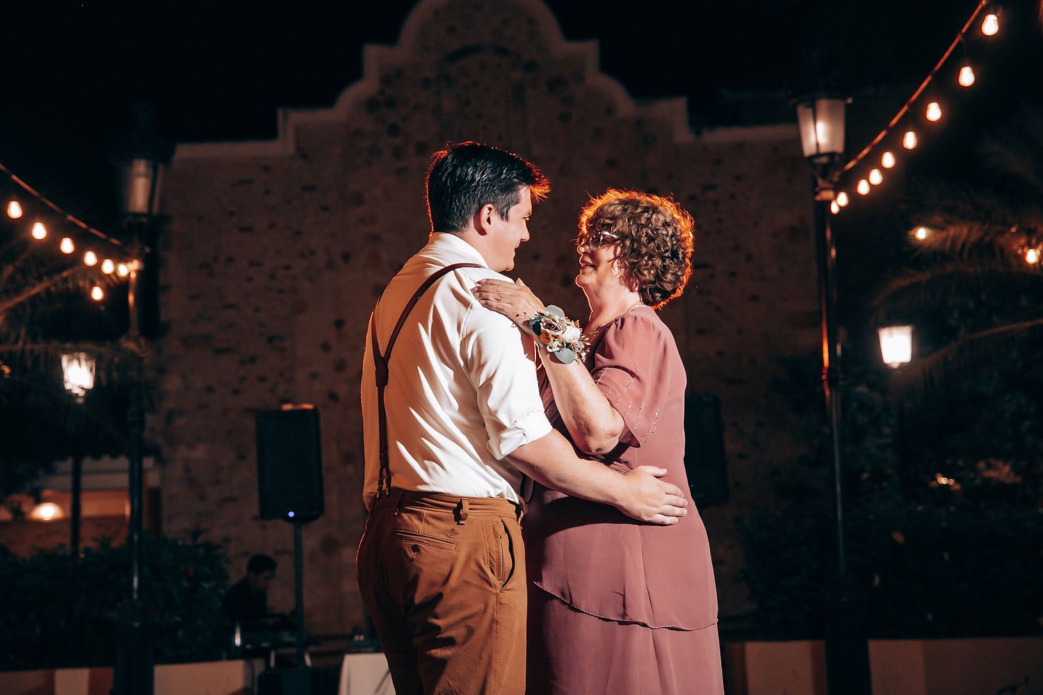 Romantic evening dance under string lights at outdoor wedding reception.