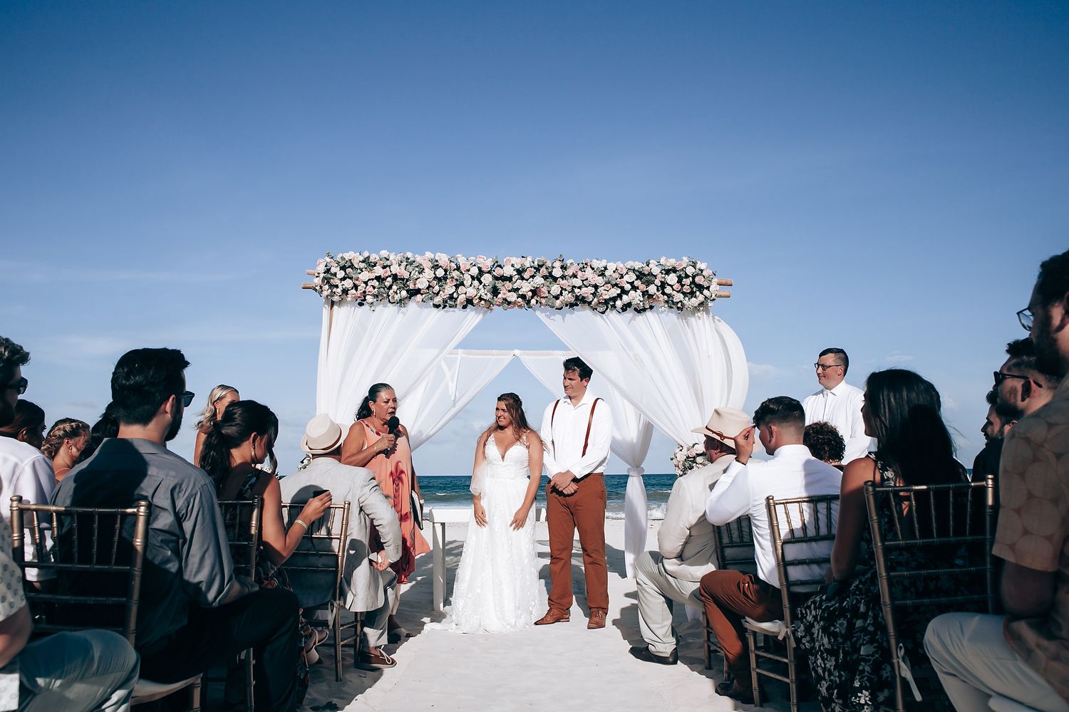 Wedding ceremony guests seated under bright blue skies with white decor elements.