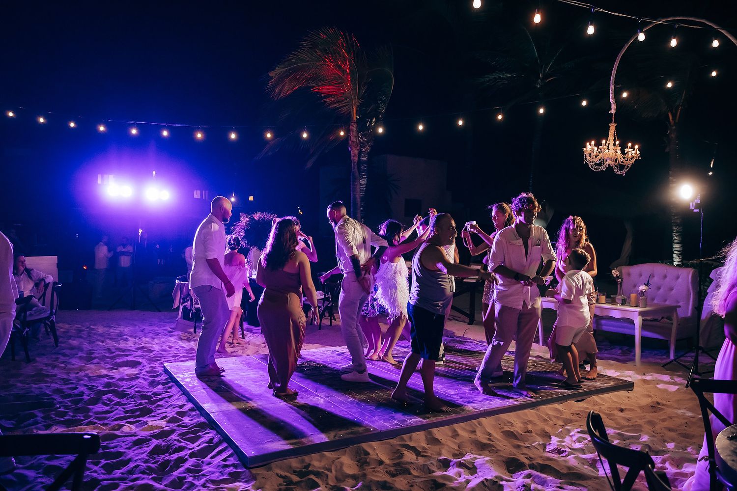 Night time wedding reception with guests dancing under purple lights and string light decorations.