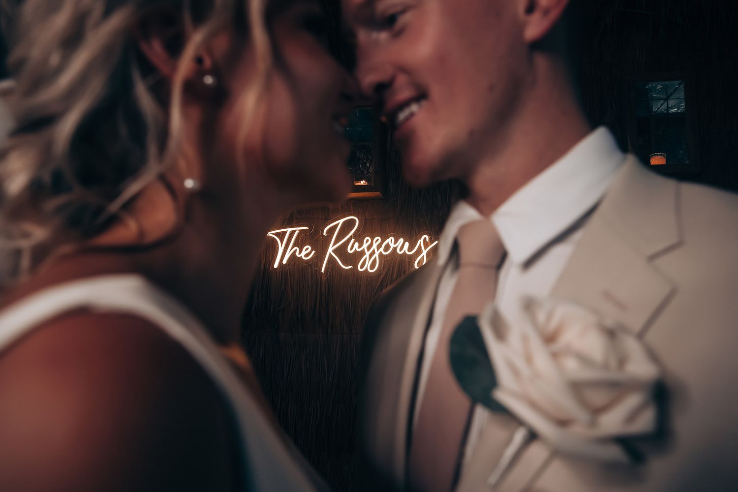 Dimly lit wedding reception scene with illuminated neon sign creating romantic ambiance.