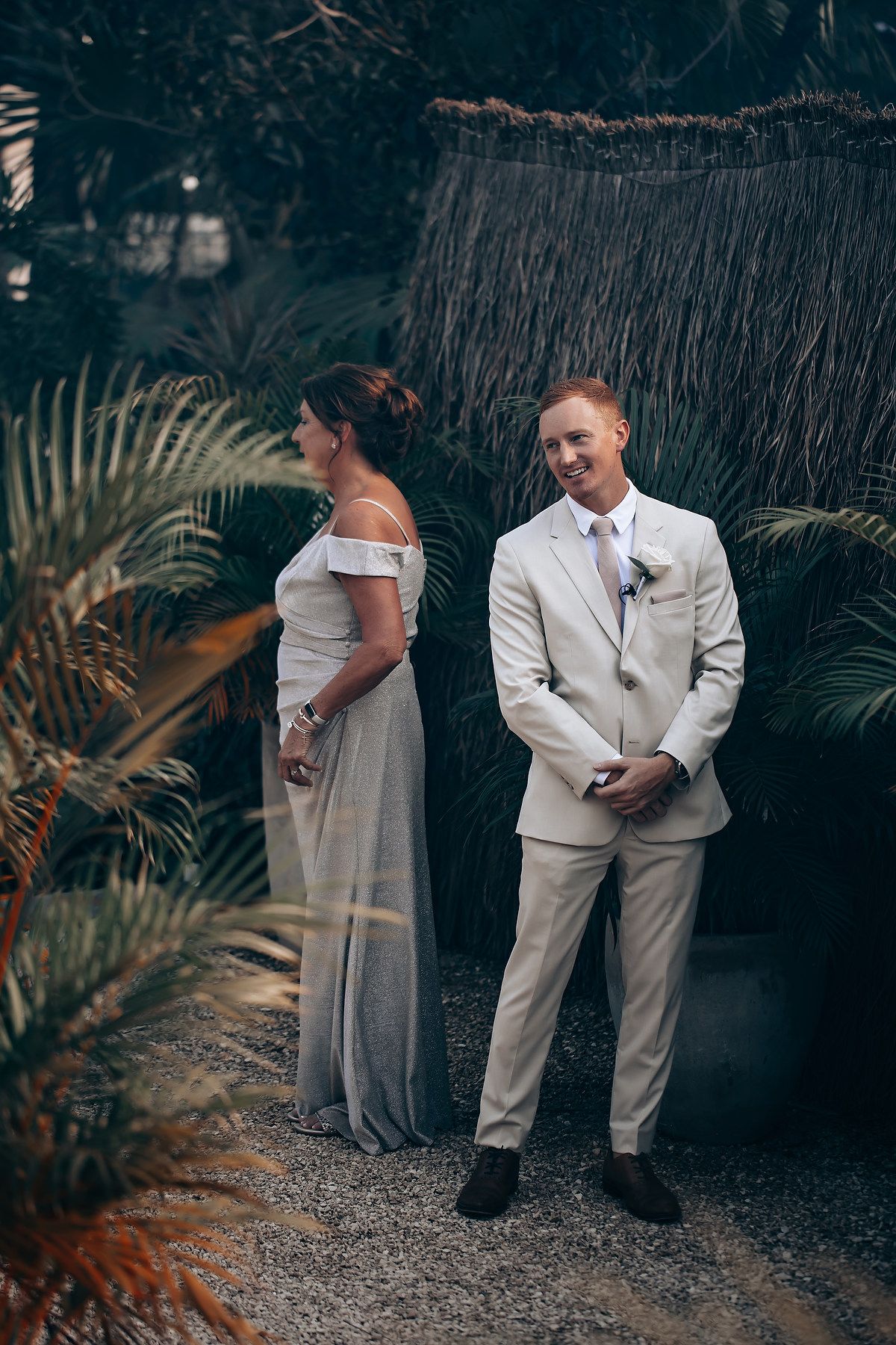 A couple shares a private moment before their wedding ceremony in a tropical garden setting with palm fronds.