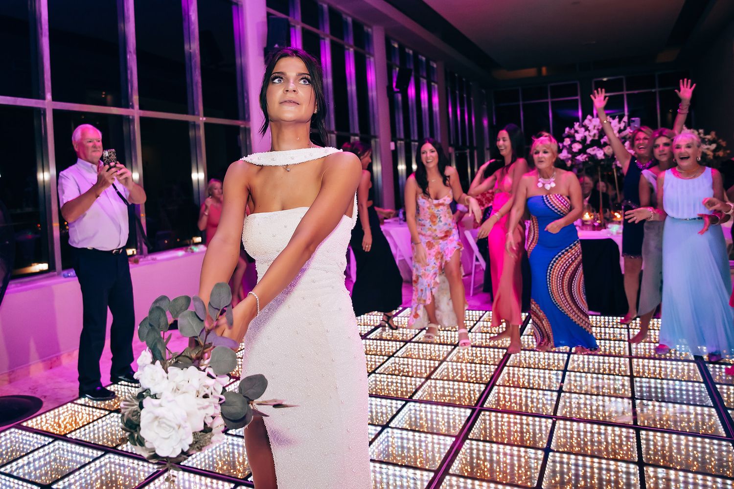 Wedding celebration on illuminated dance floor with purple ambient lighting and white decor.