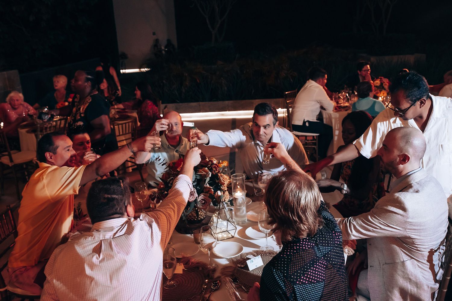 Wedding guests dance and celebrate together on a dimly lit dance floor at an indoor reception venue.