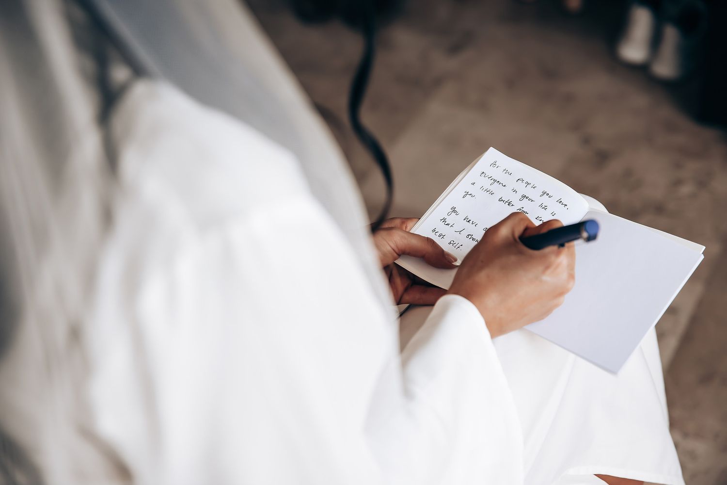 Hands holding a pen and writing on paper while wearing a white robe.