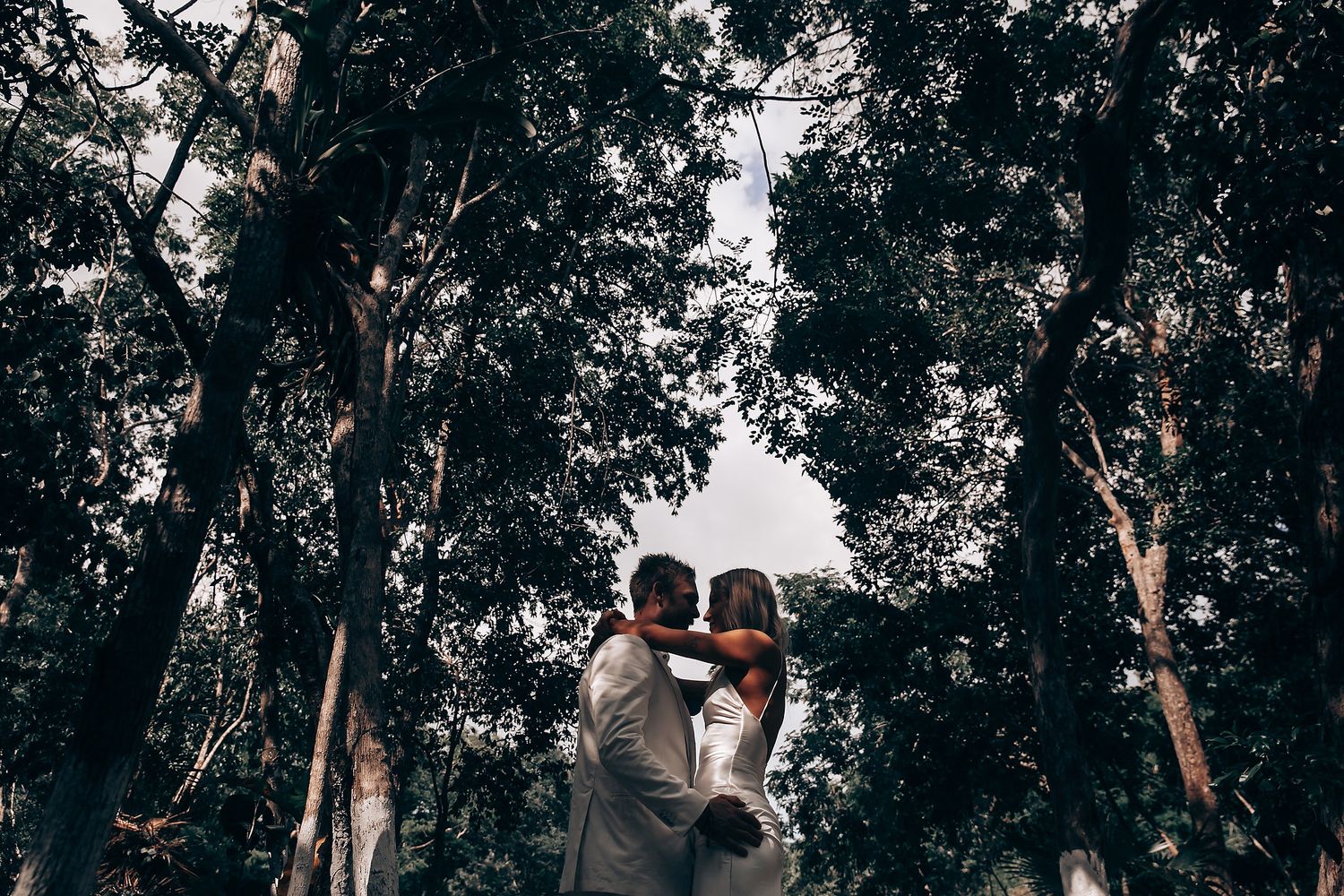 Guests celebrate during an outdoor woodland wedding ceremony surrounded by tall trees.
