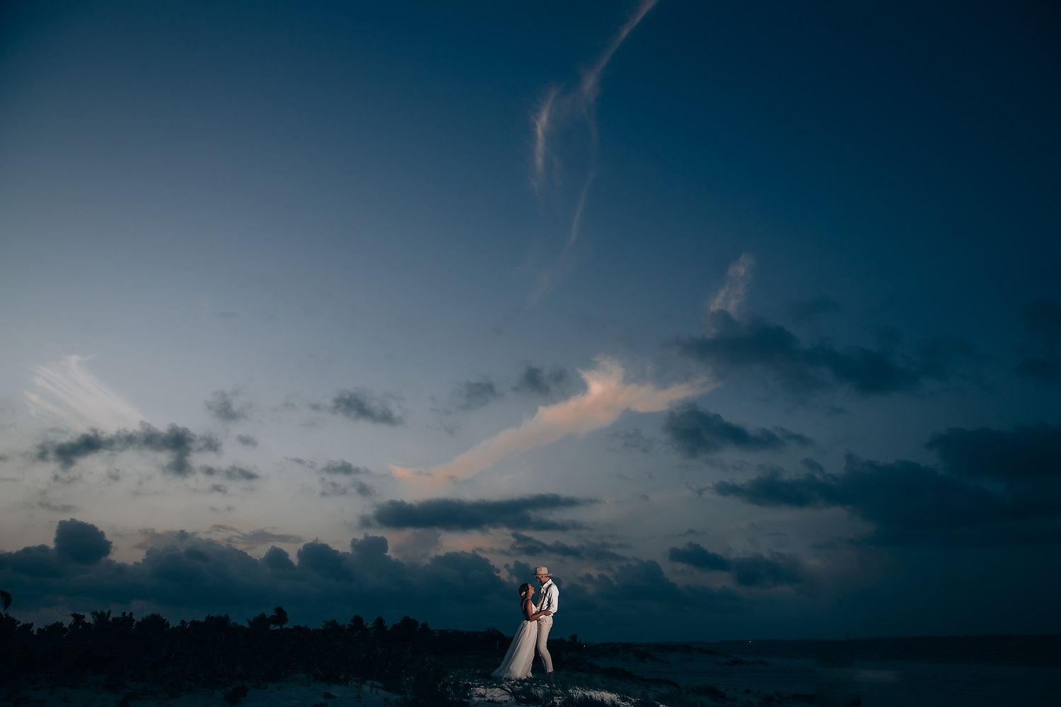 Silhouetted wedding scene against a dramatic dusk sky with deep blue and purple hues over the ocean.