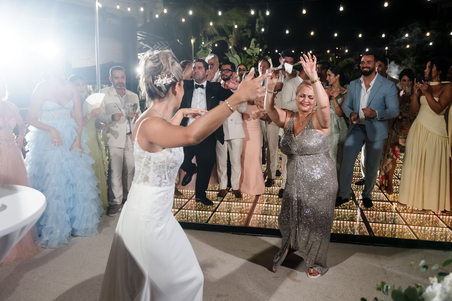 Bride and guest dancing joyfully at an outdoor wedding reception with guests celebrating in the background.