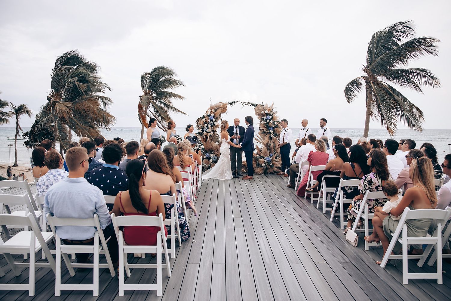 Wedding ceremony setup on a wooden deck overlooking the ocean with white chairs.