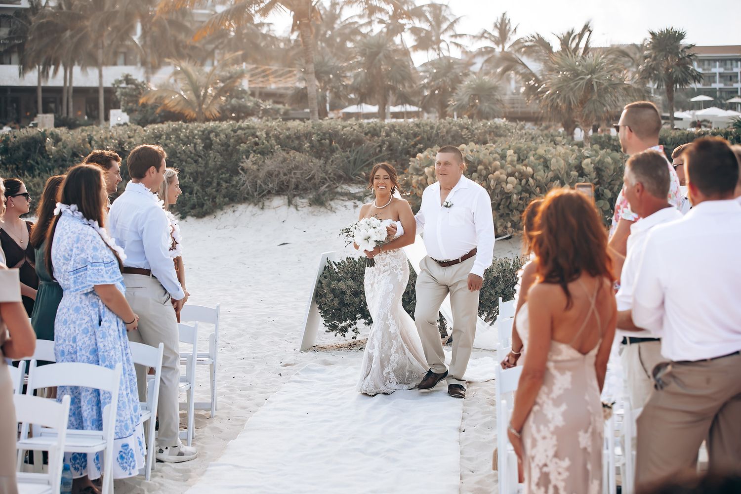 Beach wedding ceremony with white chairs and tropical palm trees in the background.