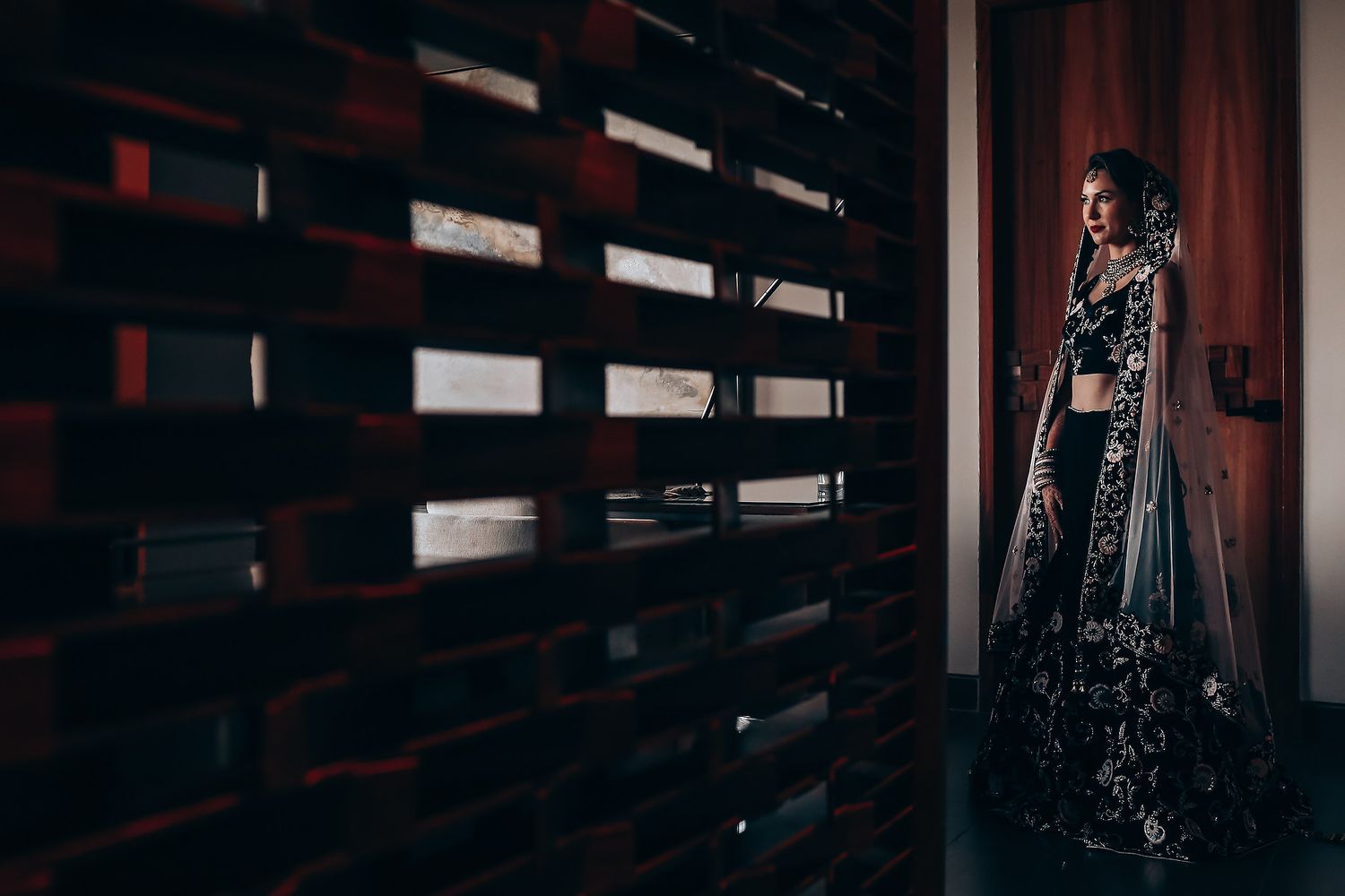 Moody silhouette of ornate South Asian wedding dress against dark interior backdrop.