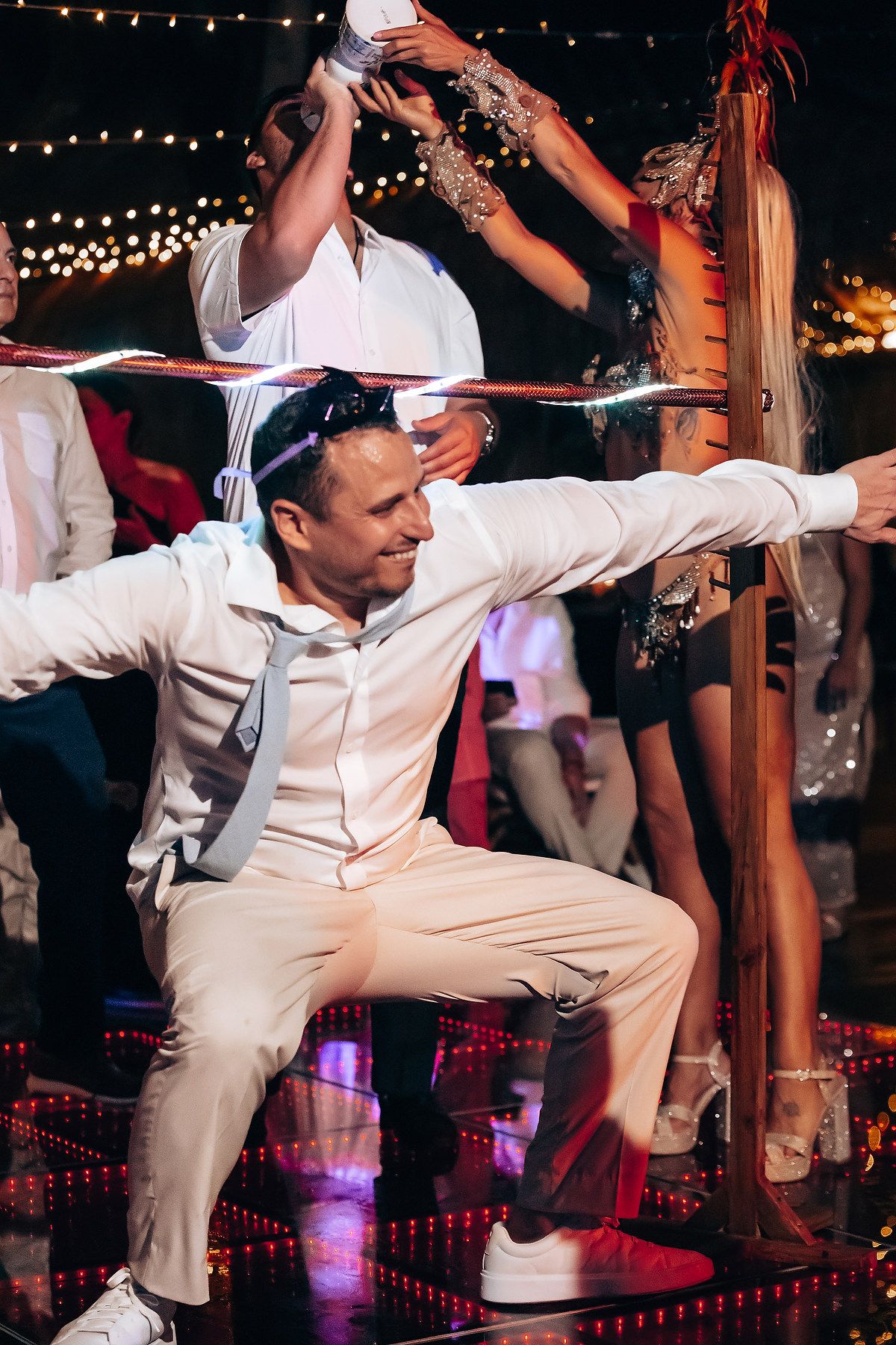 Wedding party performs synchronized dance moves under string lights at outdoor reception.