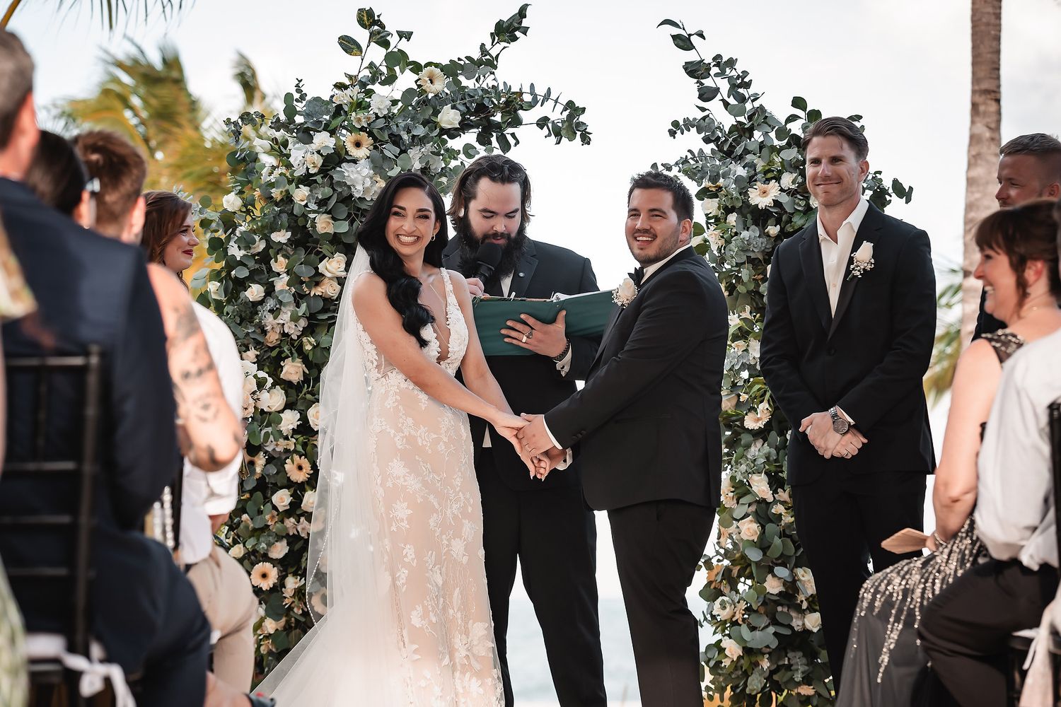 Wedding ceremony under floral arch with white roses and eucalyptus.