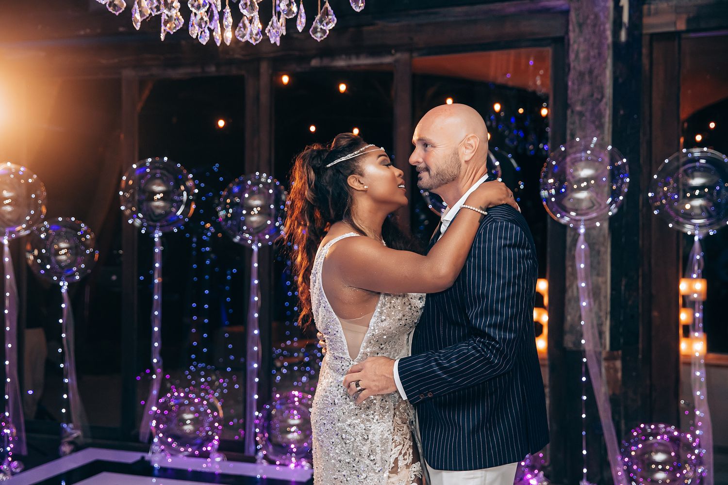 Elegant wedding reception with crystal chandeliers and romantic purple lighting creates a magical dance floor atmosphere.