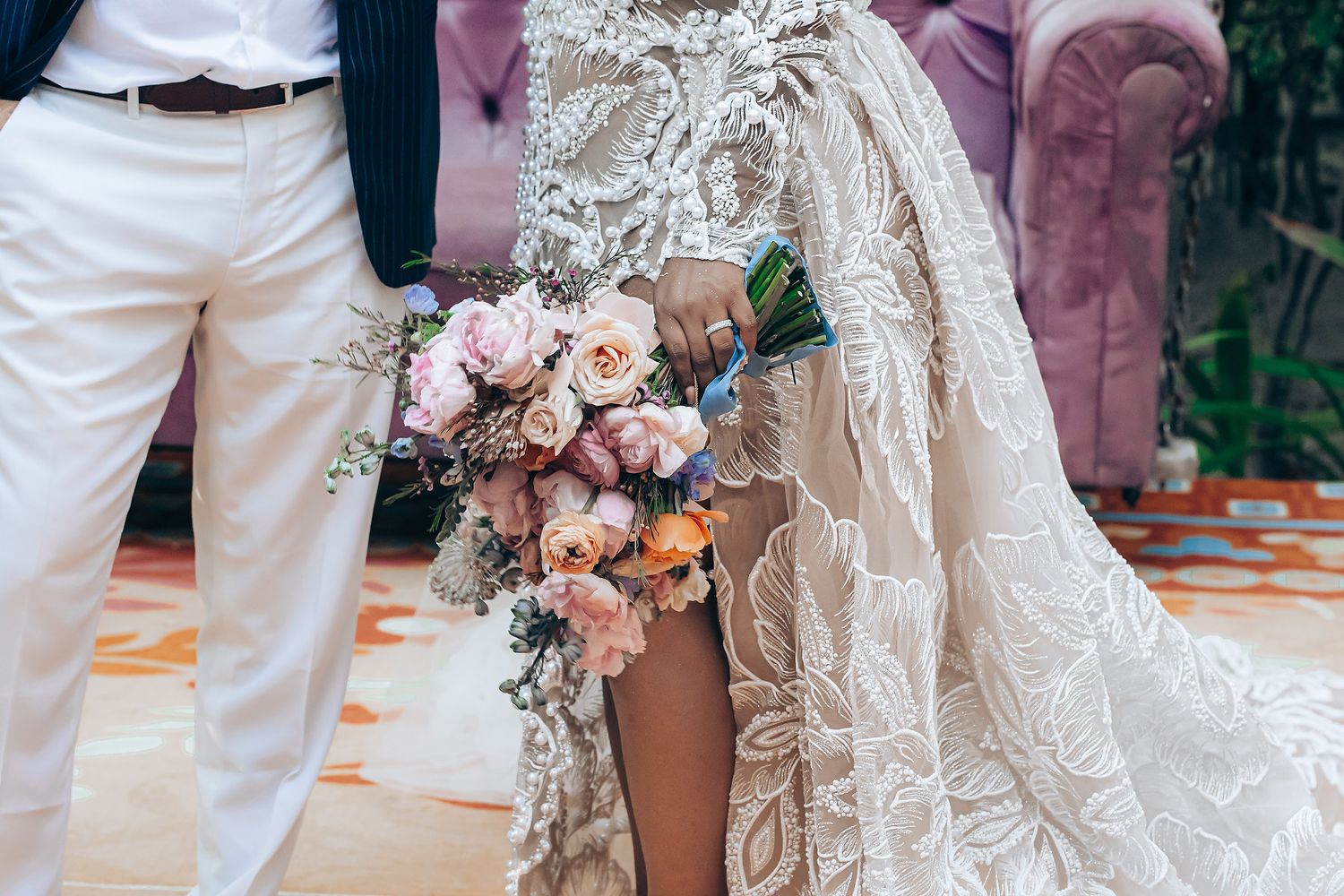 A close-up view of a bride's lace wedding dress details and floral bouquet at an outdoor ceremony.