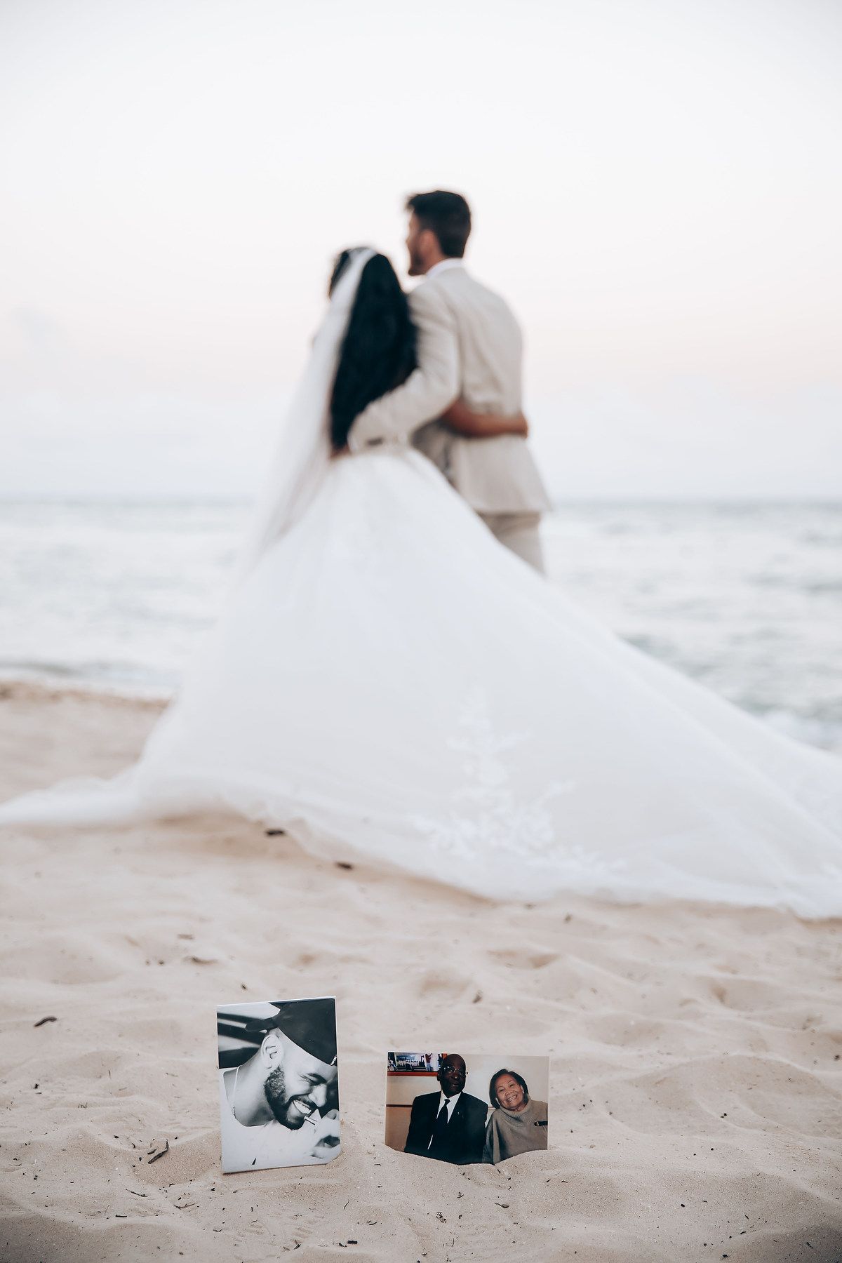 Wedding photos arranged on sandy beach with couple walking along shoreline in background.