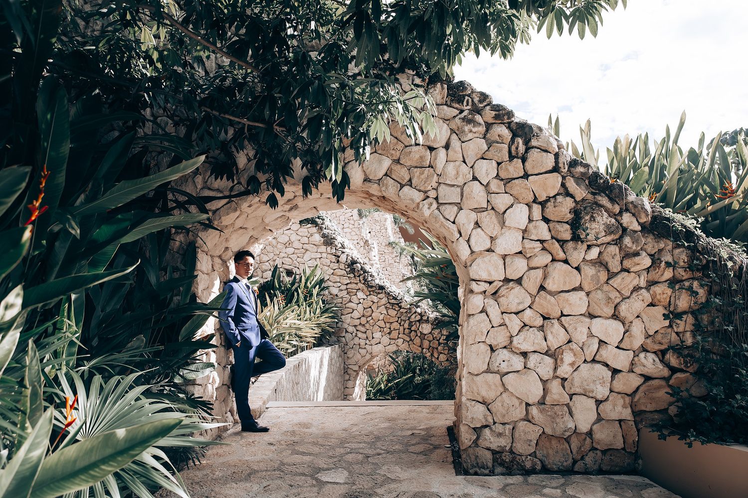 Stone wall pathway surrounded by lush tropical gardens at an outdoor wedding venue.