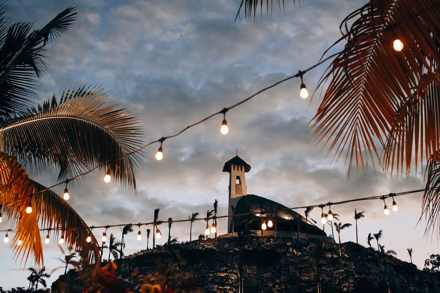 String lights hanging between palm trees at dusk creating a romantic beach wedding ambiance.