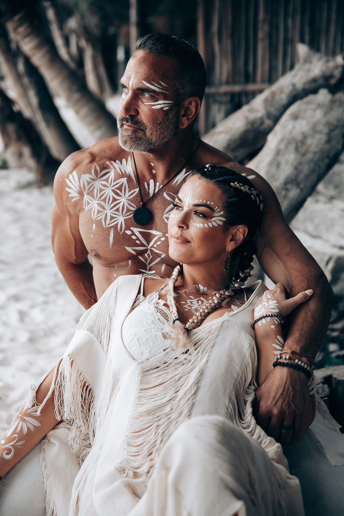 A romantic beach wedding portrait featuring white attire and decorative body paint designs.