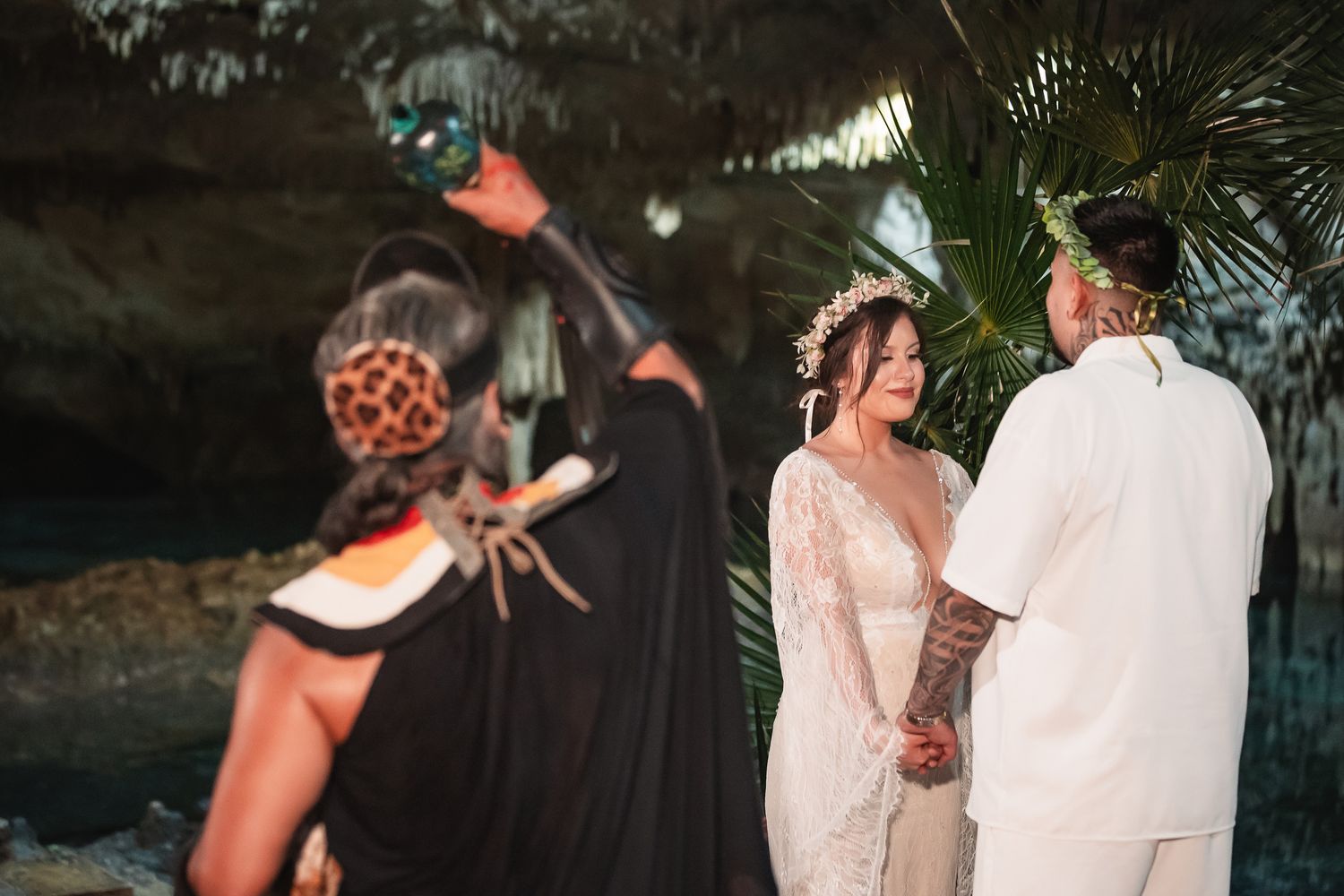 Wedding ceremony in progress within a naturally lit cave surrounded by tropical decorations.