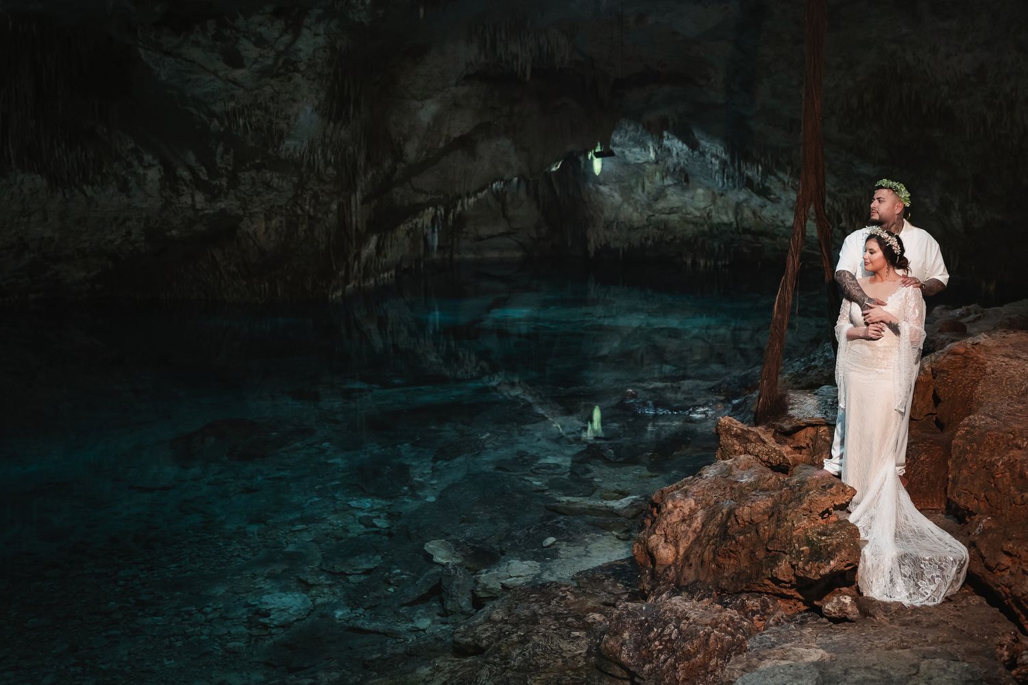 A romantic wedding portrait in a dramatic cave setting with ethereal blue water.