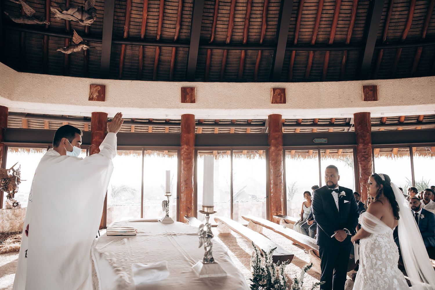 Wedding ceremony in progress inside a rustic wooden barn venue with natural light streaming through windows.