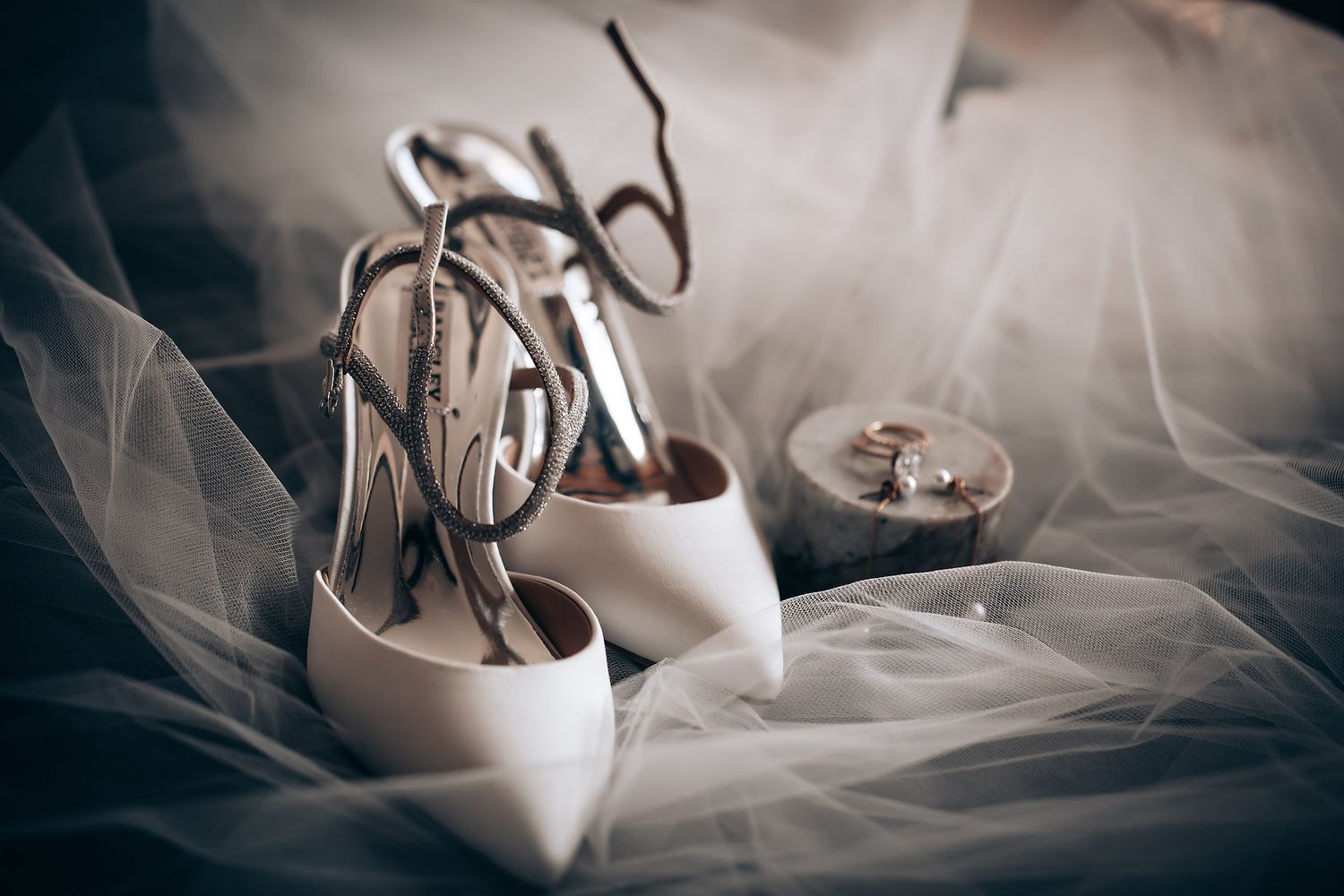 Elegant white bridal shoes with delicate straps displayed on tulle fabric.