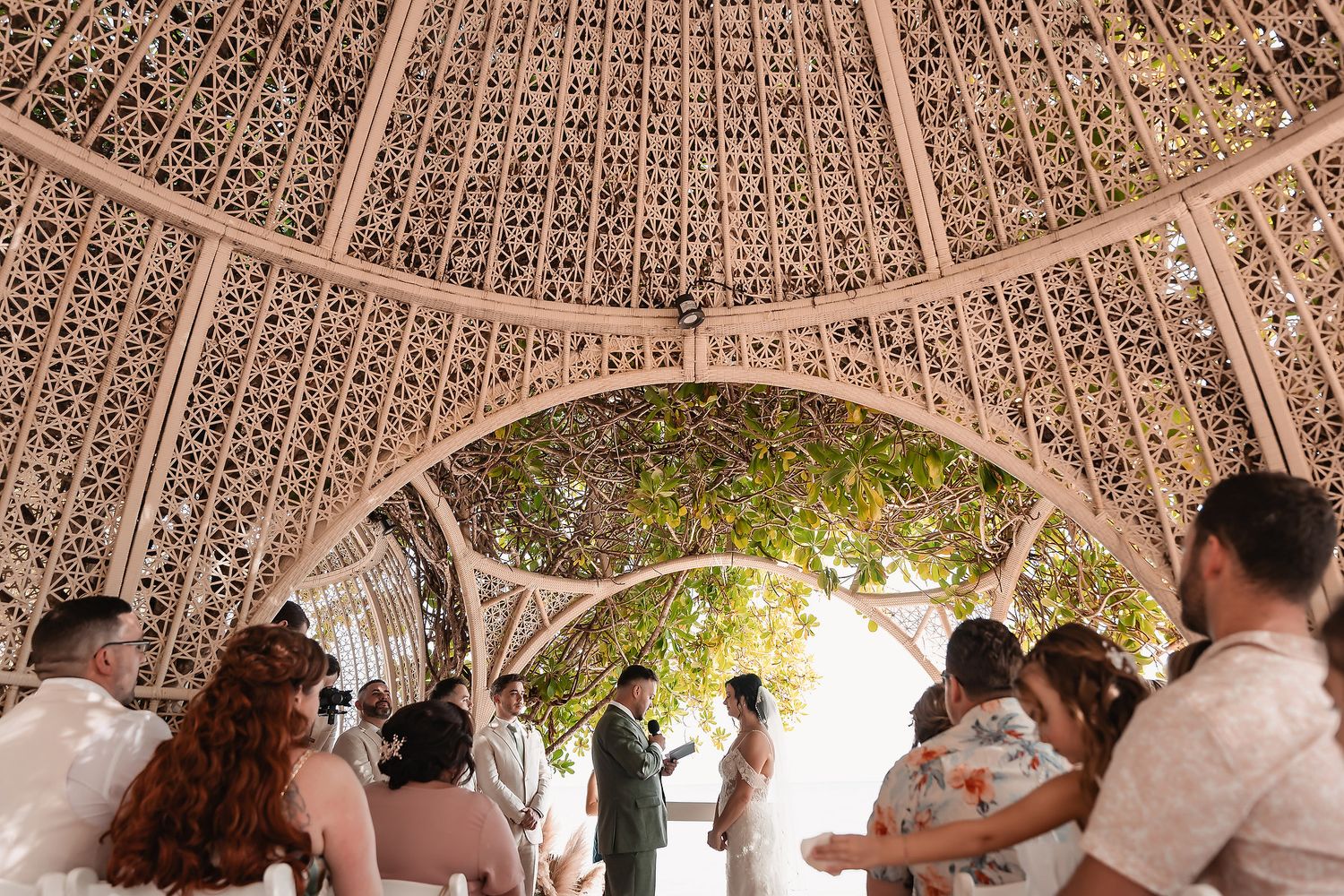 Guests celebrating at an outdoor wedding reception under a decorative wooden pergola.
