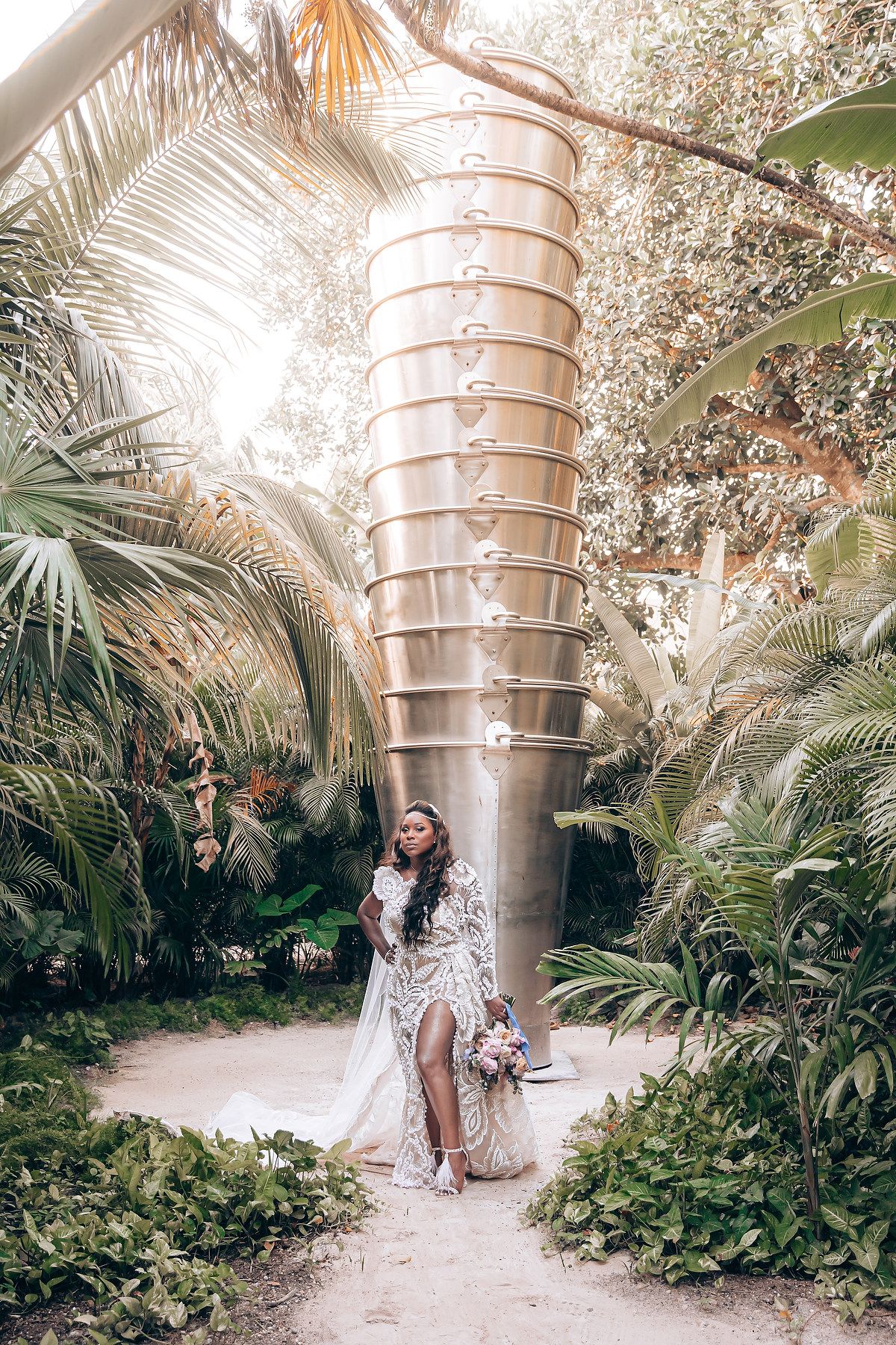 Wedding photoshoot in a tropical garden with towering metallic sculptures and palm trees.