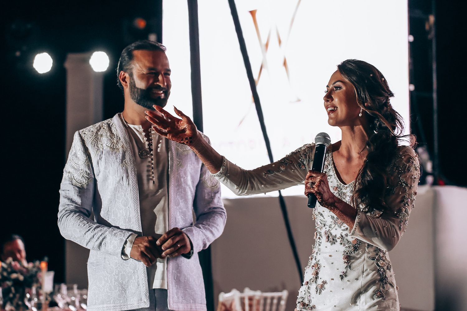 Newlywed couple shares their first dance together at an elegant evening wedding reception with dramatic lighting.