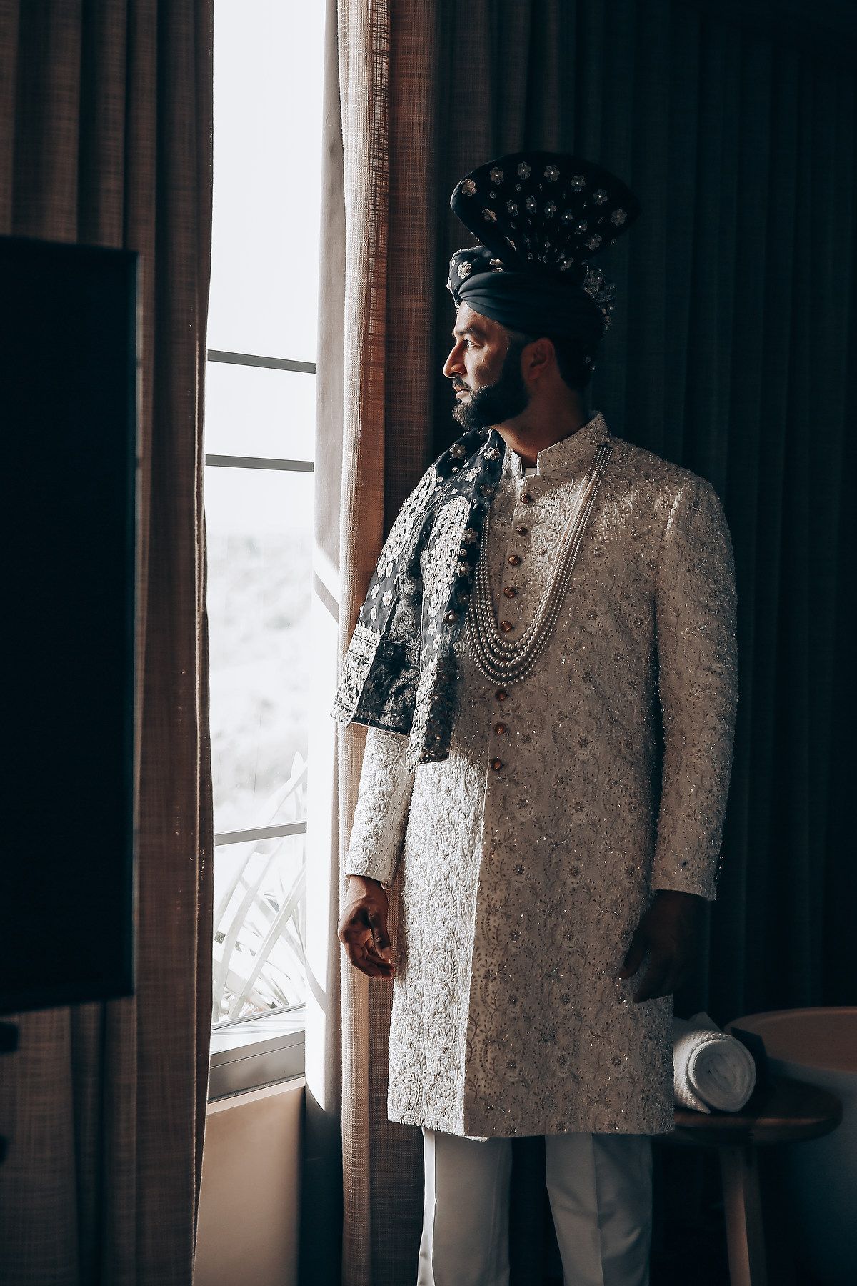 Elegant white and cream formal attire photographed in dramatic indoor lighting by a window.